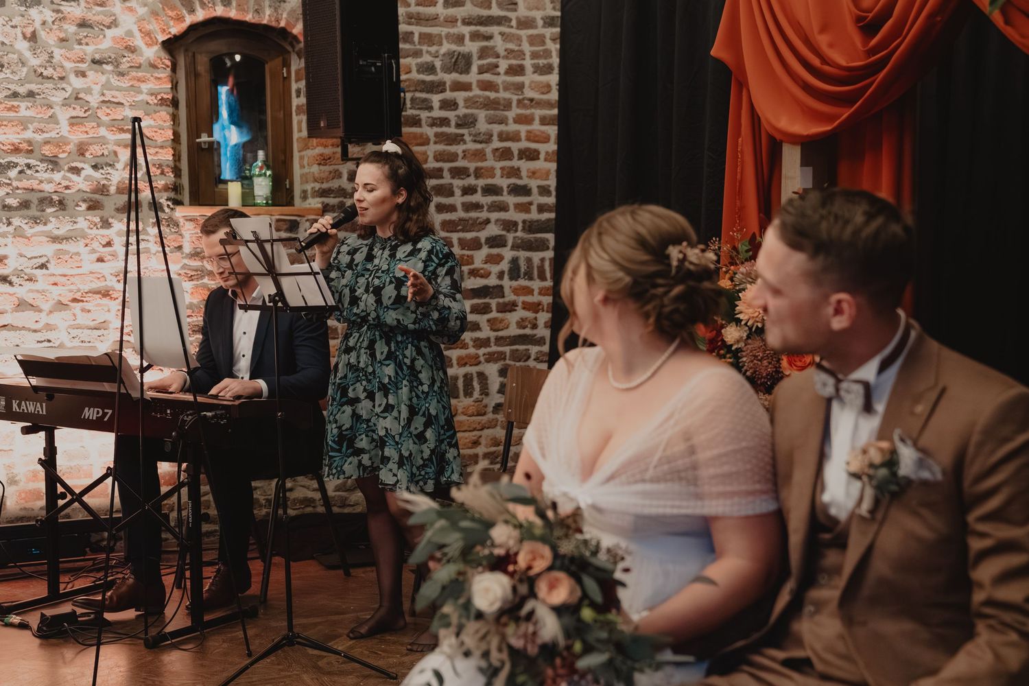 Wedding reception in rustic brick venue with warm lighting and orange drapery.