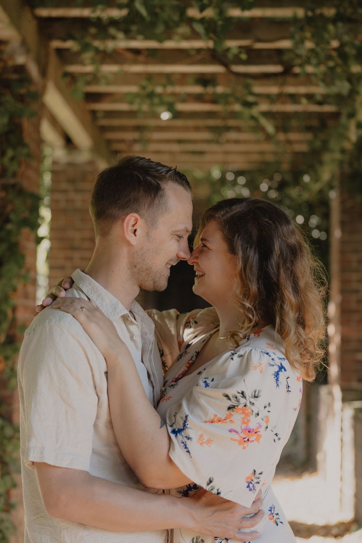 Romantic couple embracing under wooden pergola with climbing vines.