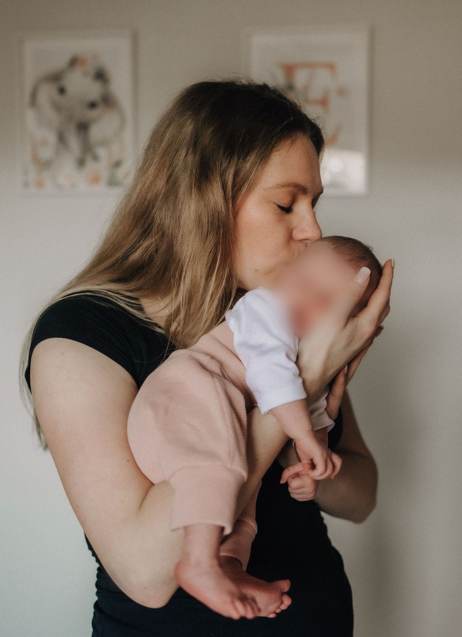 A tender moment captured as a parent in black shirt holds and kisses a baby wearing soft pink and white clothing.