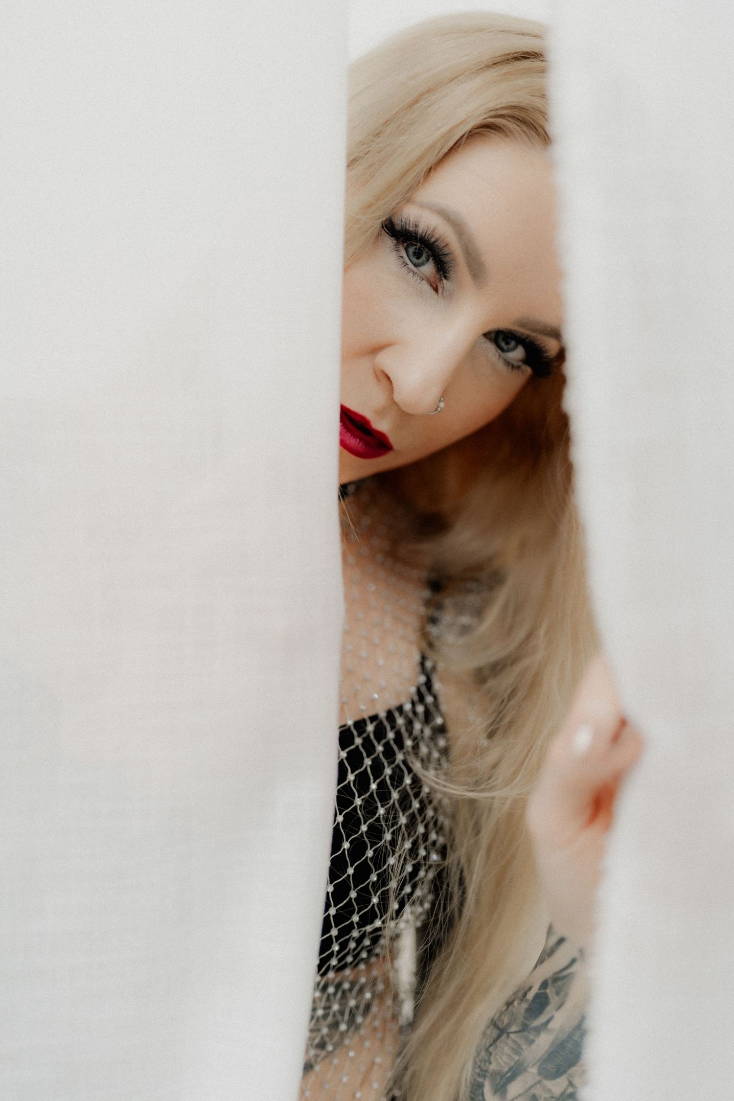 Artistic portrait with dramatic makeup, blonde hair, and fishnet details against a white background.