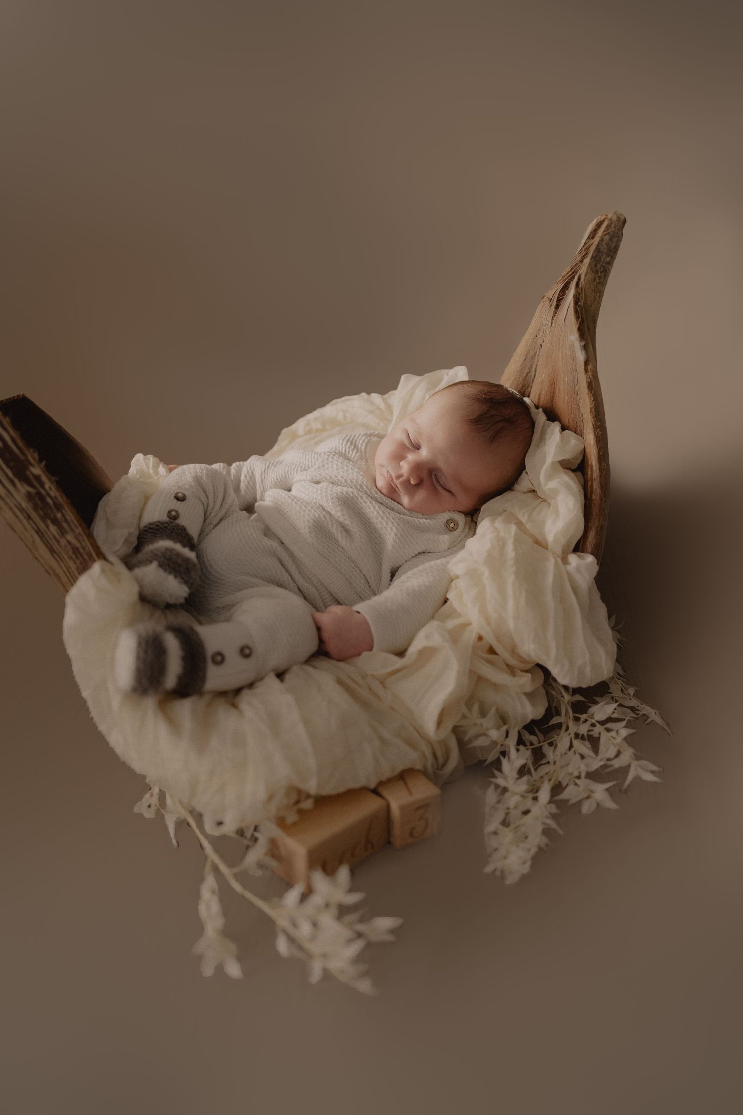 A sleeping baby in white clothing lies on a textured blanket in soft, moody lighting.