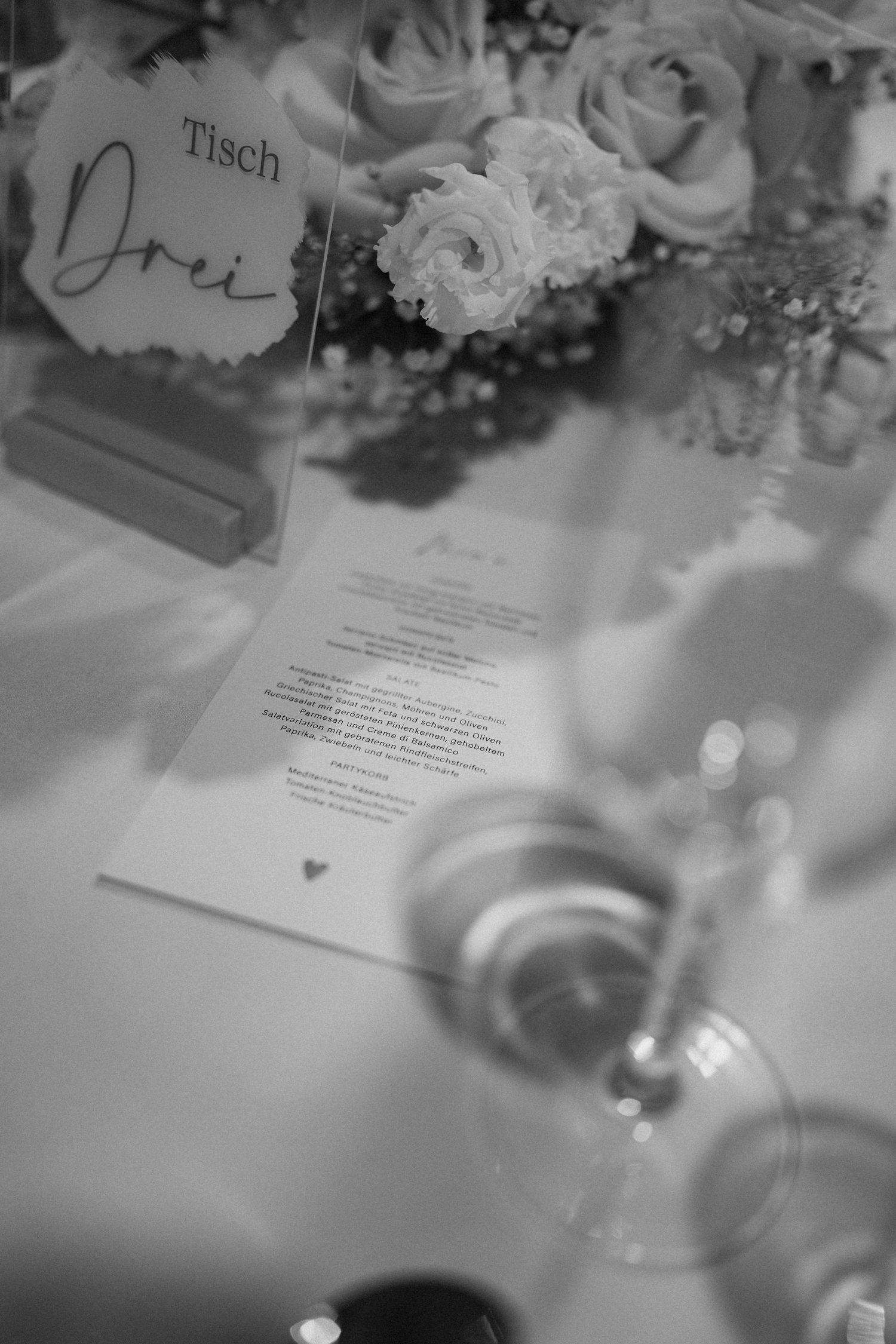 Black and white detail of wedding table setting with roses and menu card.