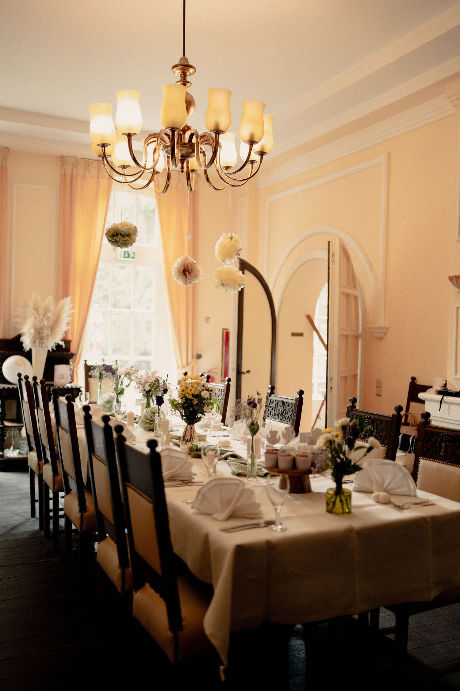 Elegant dining room with chandelier, long table set for a baby shower event with white linens and floral centerpieces.