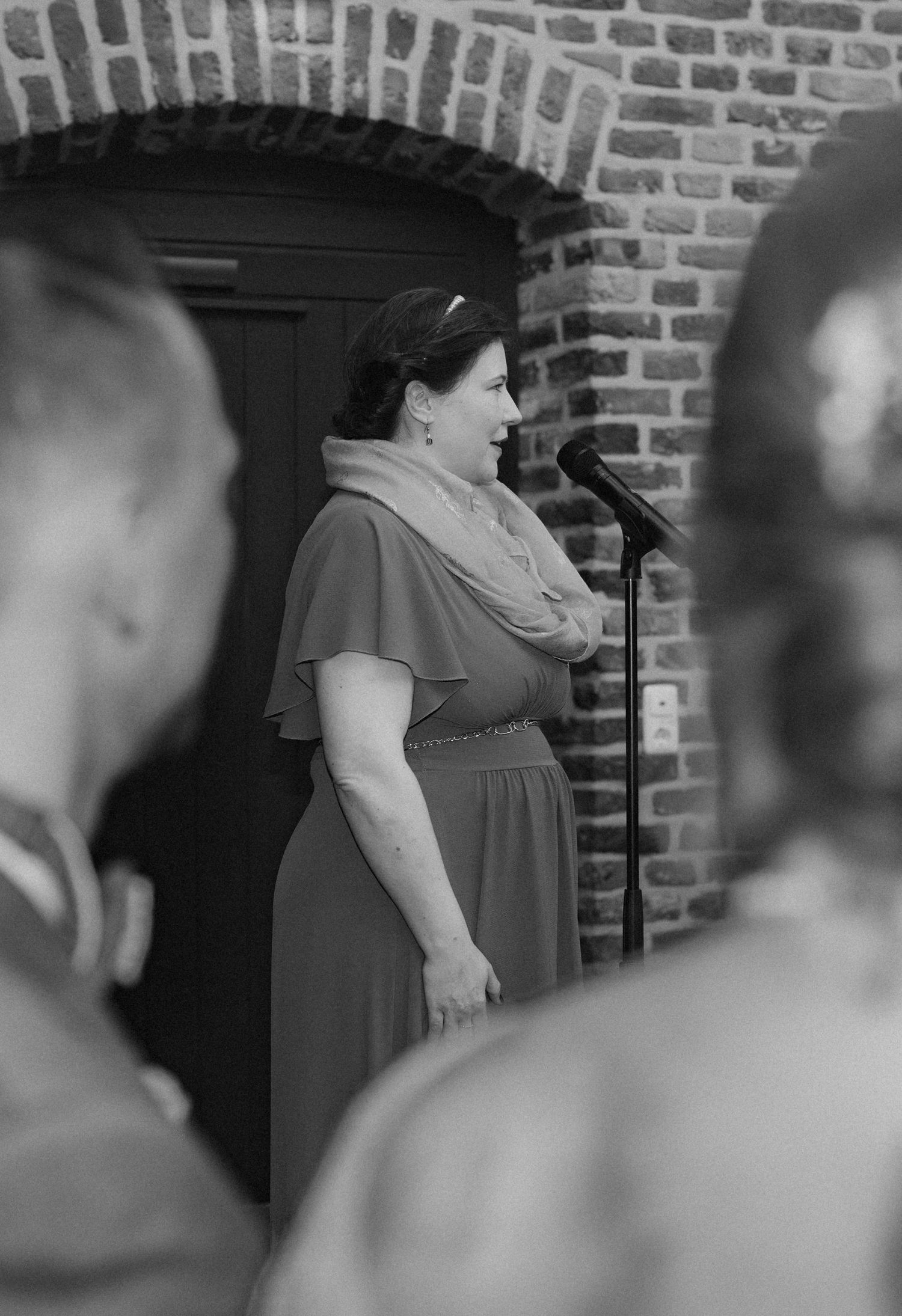 Black and white photo of wedding ceremony attendees in a brick-walled venue.