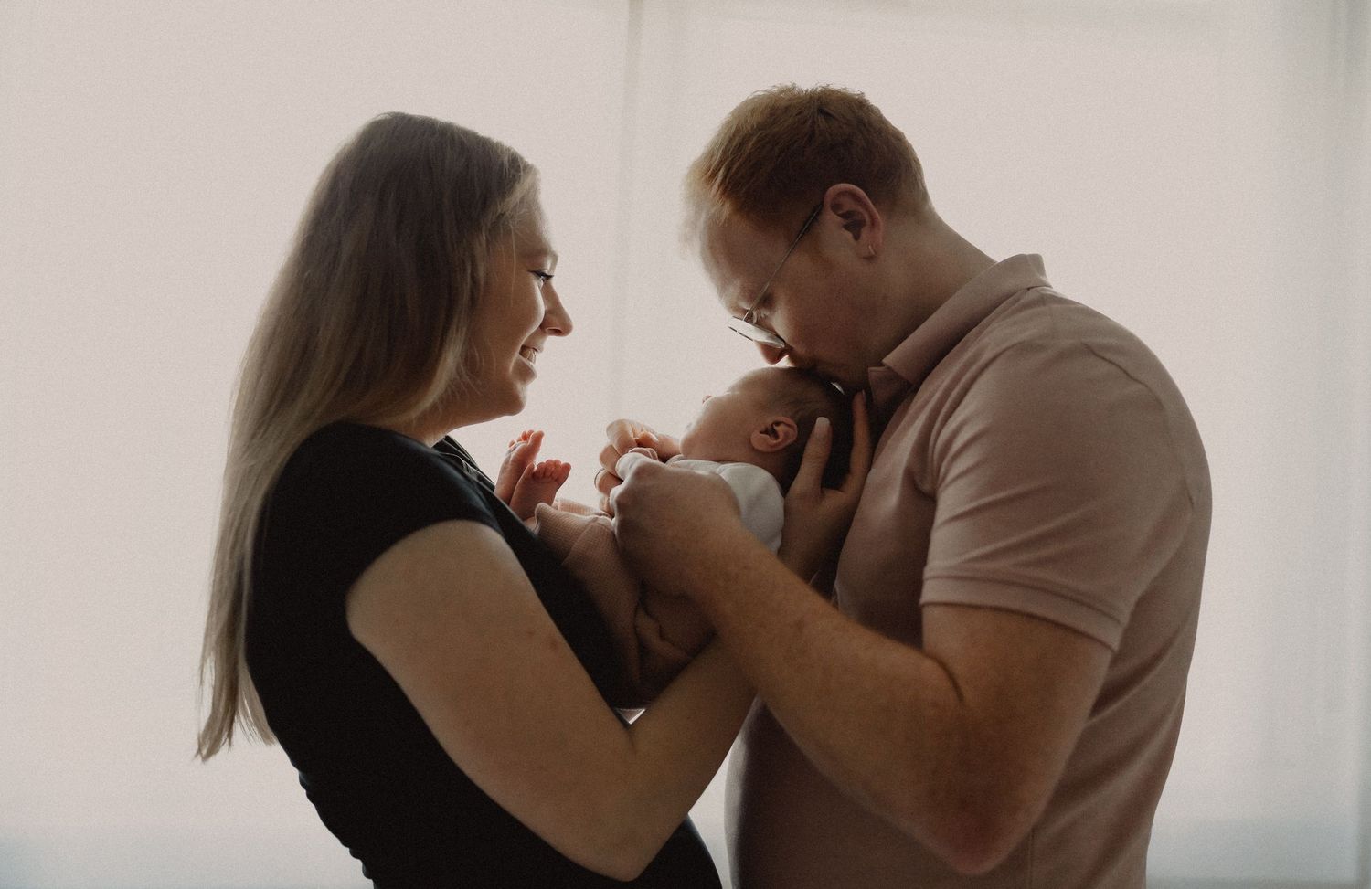A tender moment between two people in soft lighting as they gaze down lovingly at their newborn baby.
