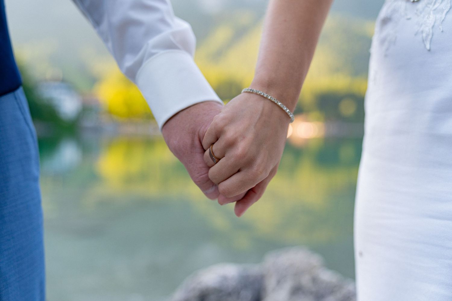 Couple holding hands during a romantic wedding ceremony by a scenic mountain lake.