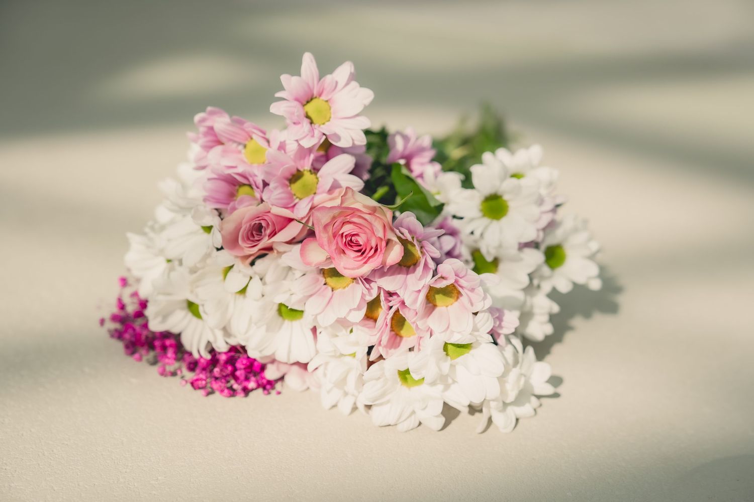 A beautiful bouquet of pink roses, white chrysanthemums, and colorful wildflowers arranged on a soft white surface.