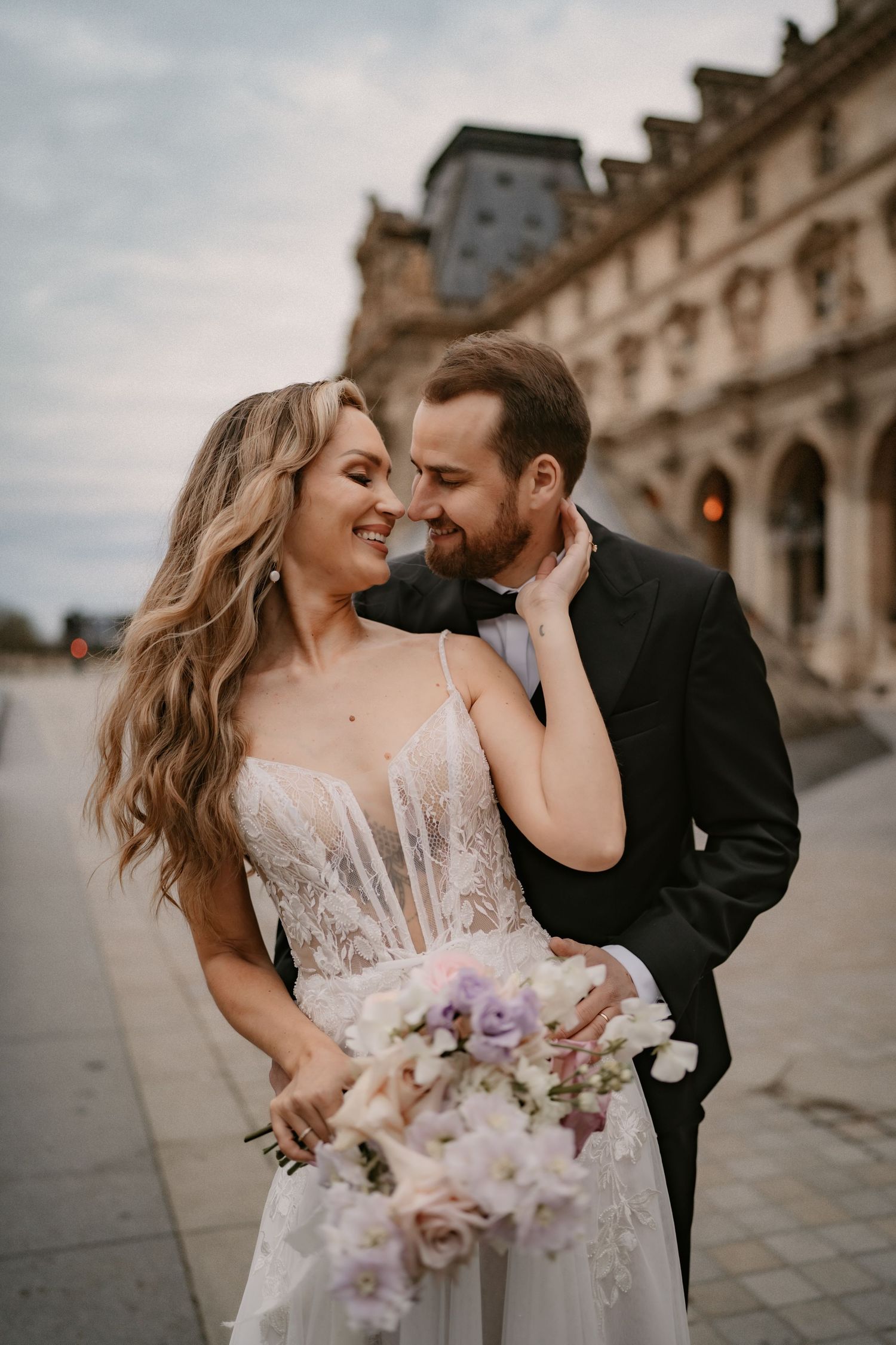 Intimate wedding portrait with couple laughing together while holding purple and white bouquet.