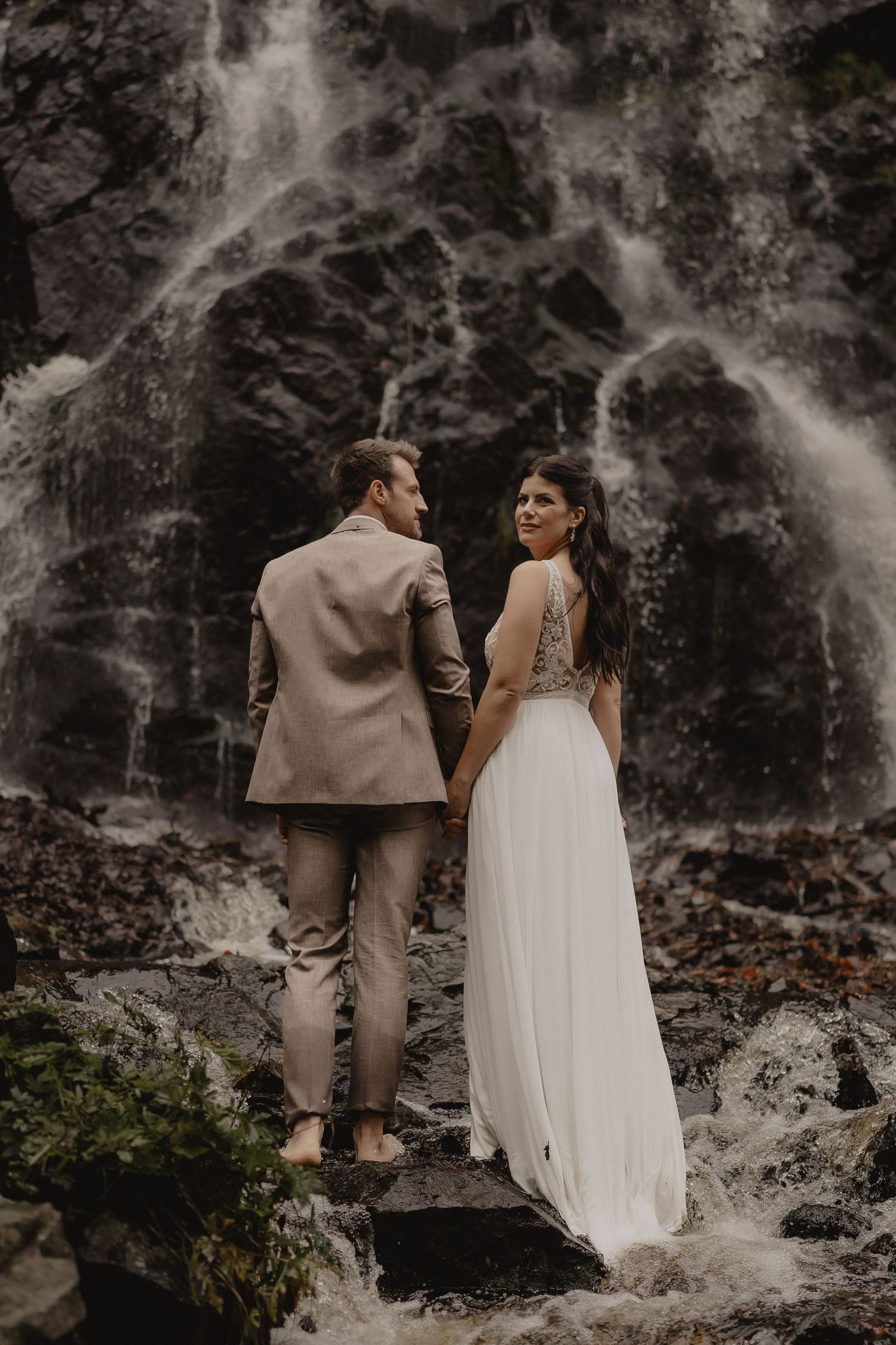 Romantic couple poses near a misty waterfall in a moody black and white photoshoot.