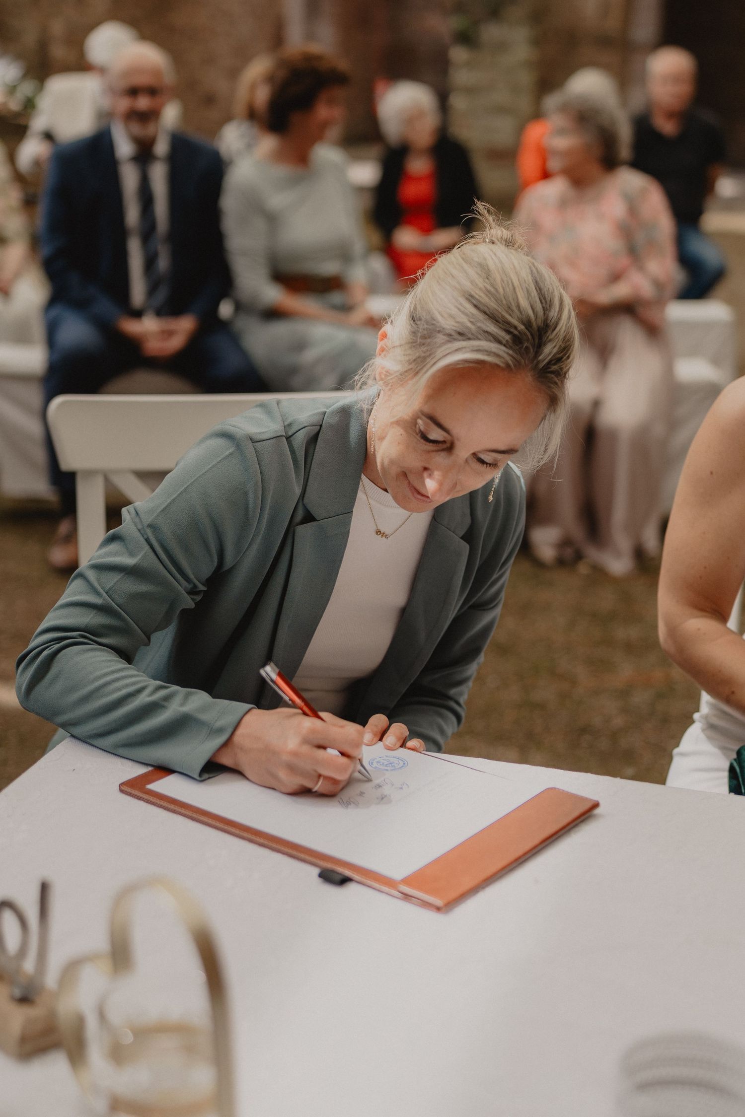 Wedding guest in a gray blazer signs official documents at a white table during the ceremony.