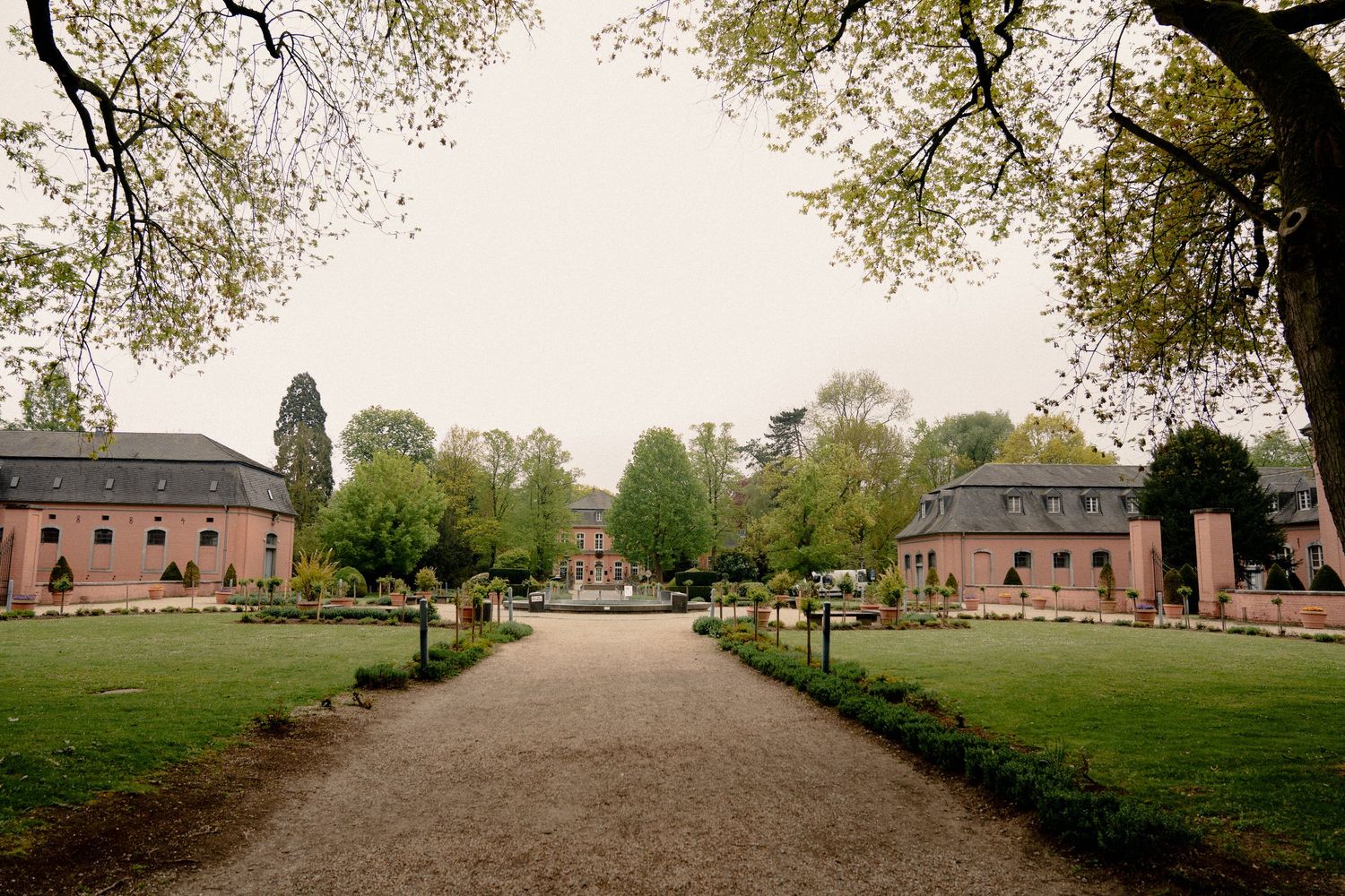 Symmetrical garden path leading to a historic brick manor house flanked by trees and manicured lawns.