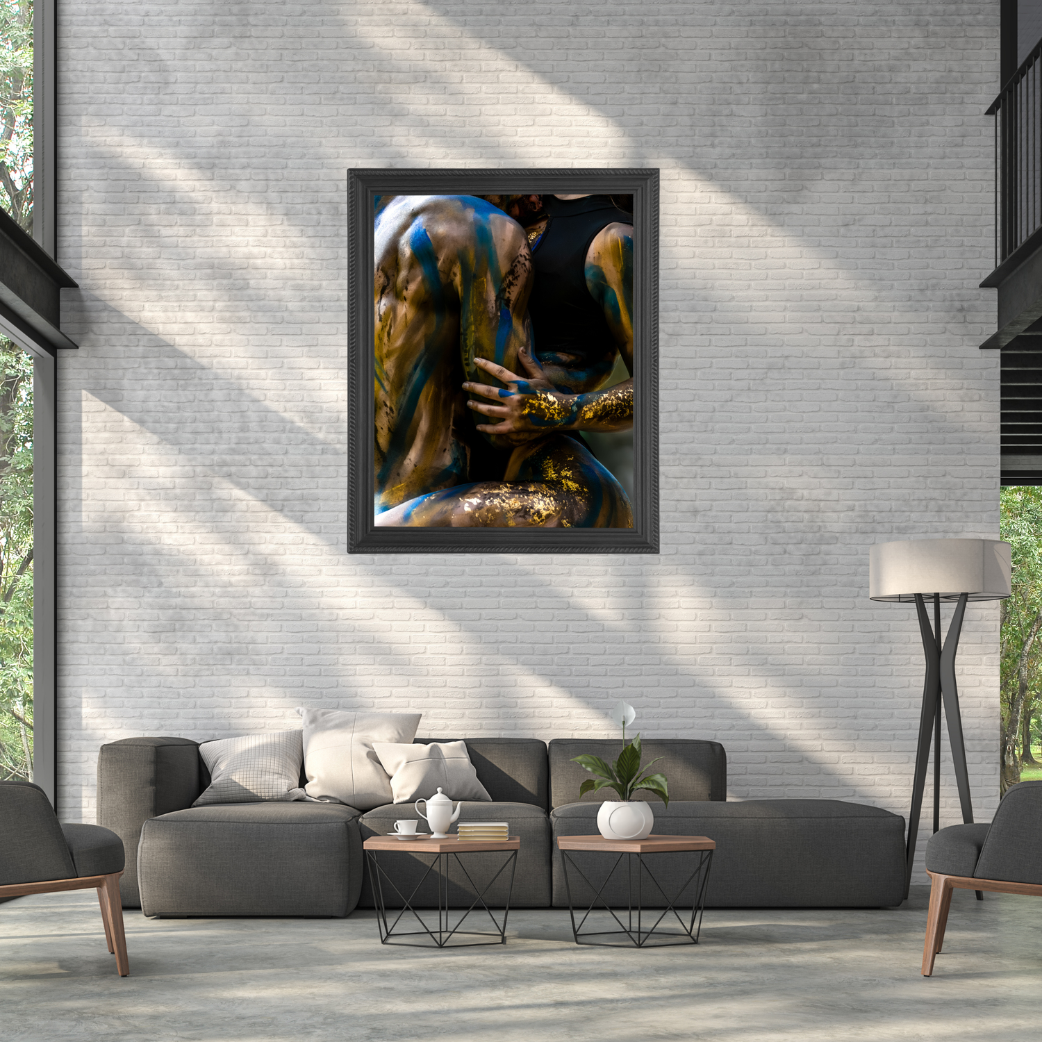Framed wall art of a figure with gold and blue body paint displayed above a modern gray sofa in a loft living room.