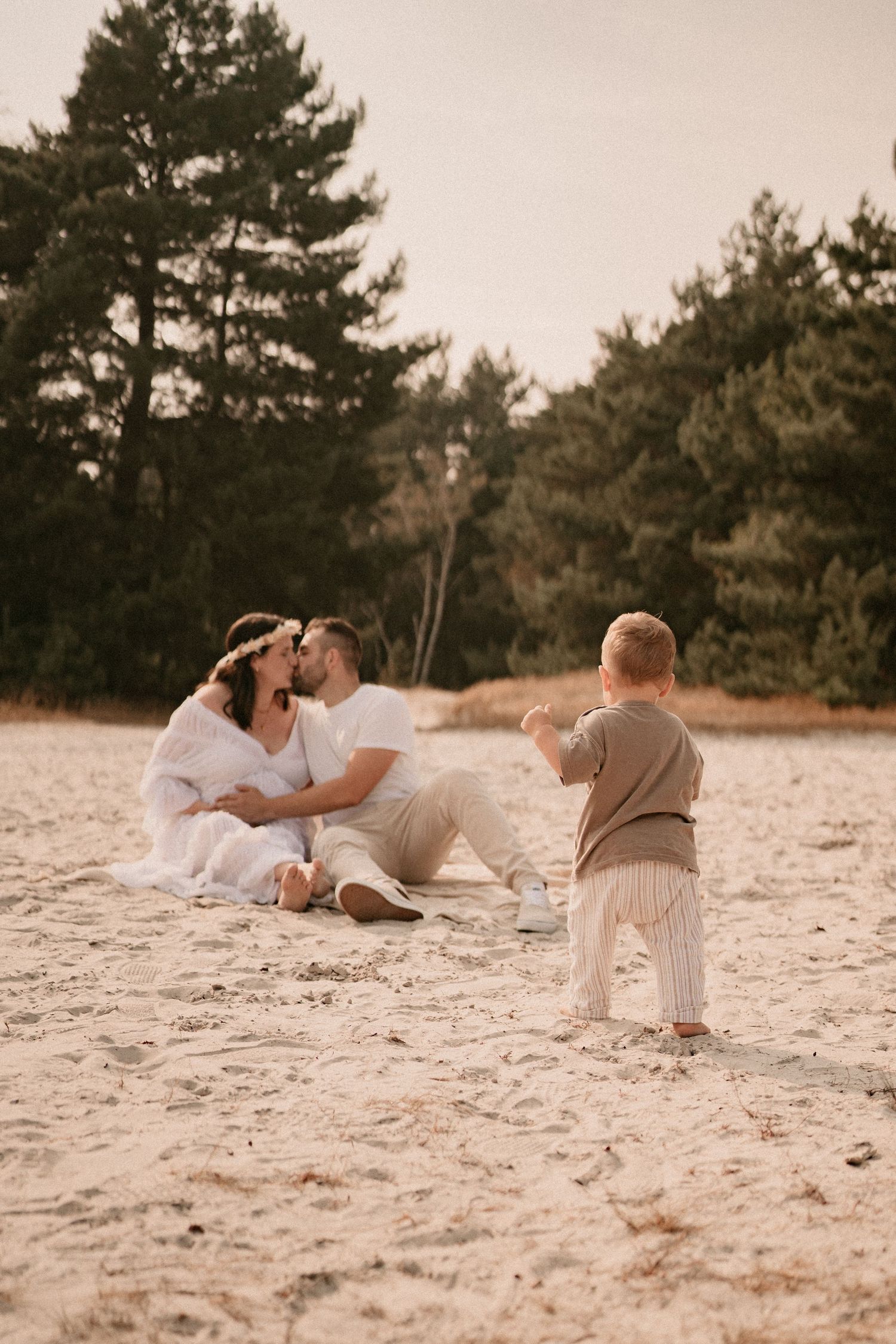 A family relaxes together on white sand with evergreen trees creating a natural backdrop.