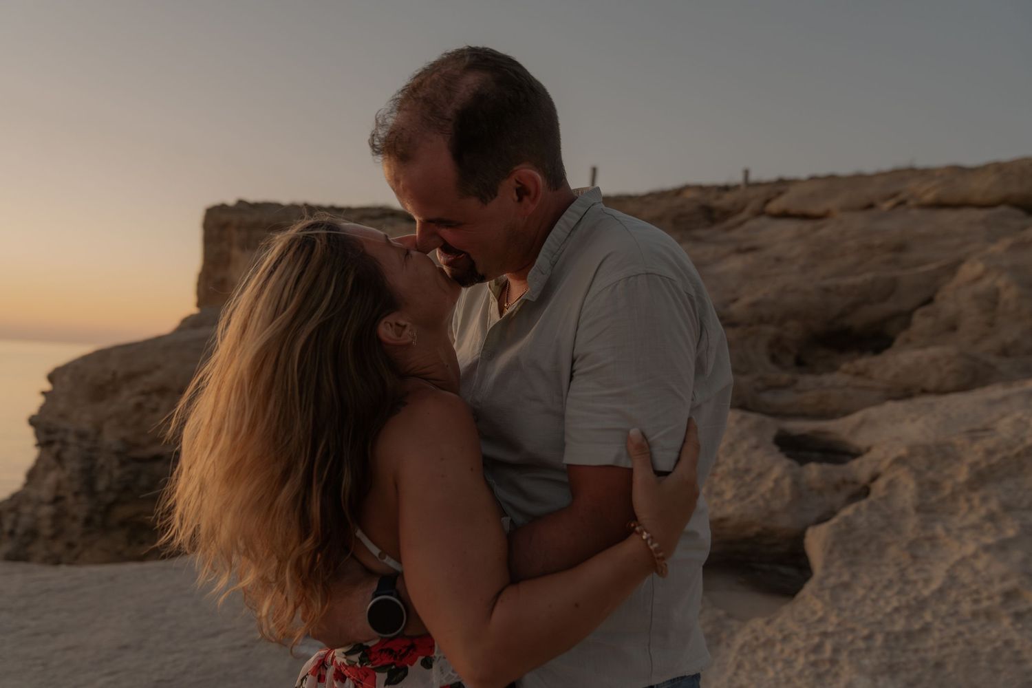 Couple embracing against dramatic coastal sunset backdrop.