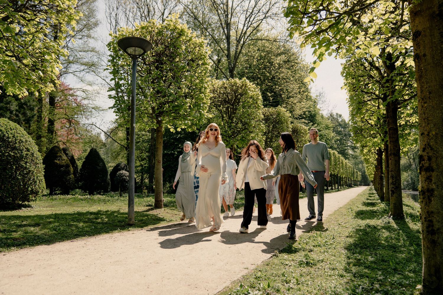 Group of friends walking together along a sunny tree-lined park pathway in spring.