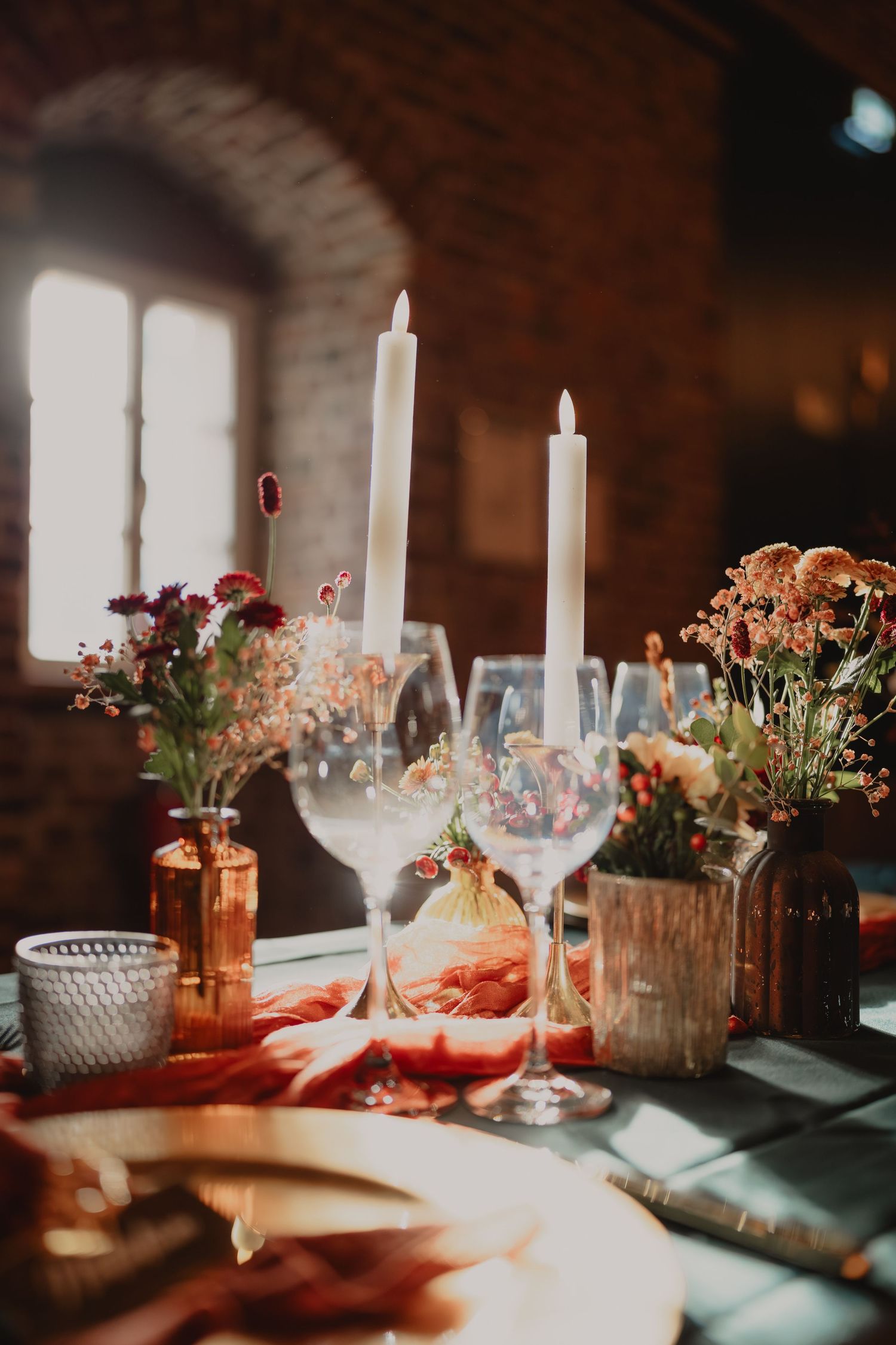 Elegant wedding table setting with white candles, floral centerpieces, and glassware in rustic brick venue.