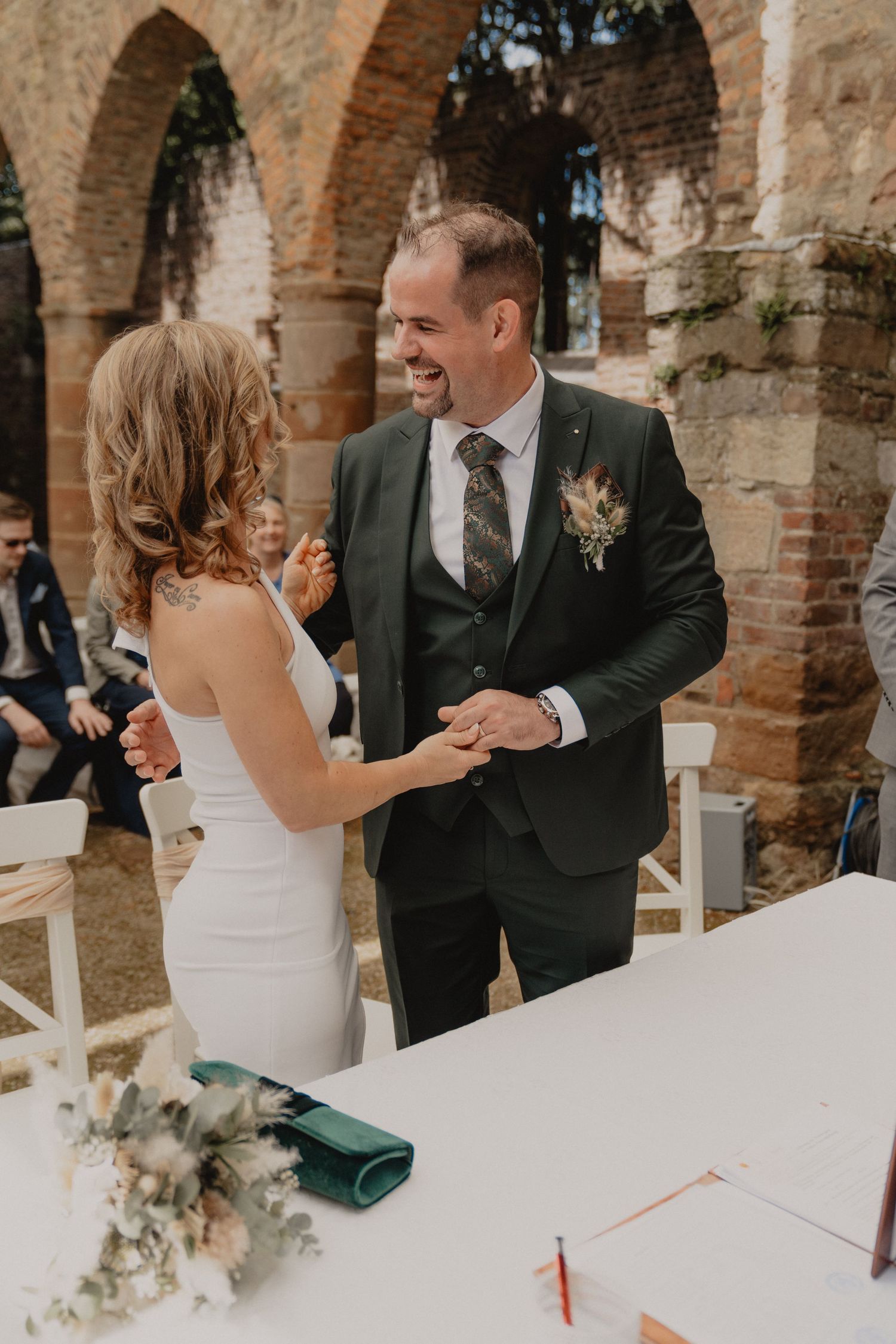 Joyful wedding ceremony moment captured under rustic brick archways with white chairs and floral decorations.
