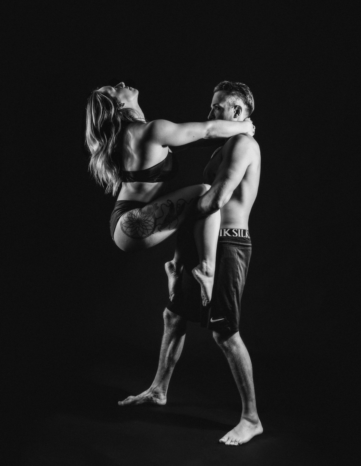 Black and white photo of a man and woman dancing together, with the woman lifting her leg in an athletic pose.