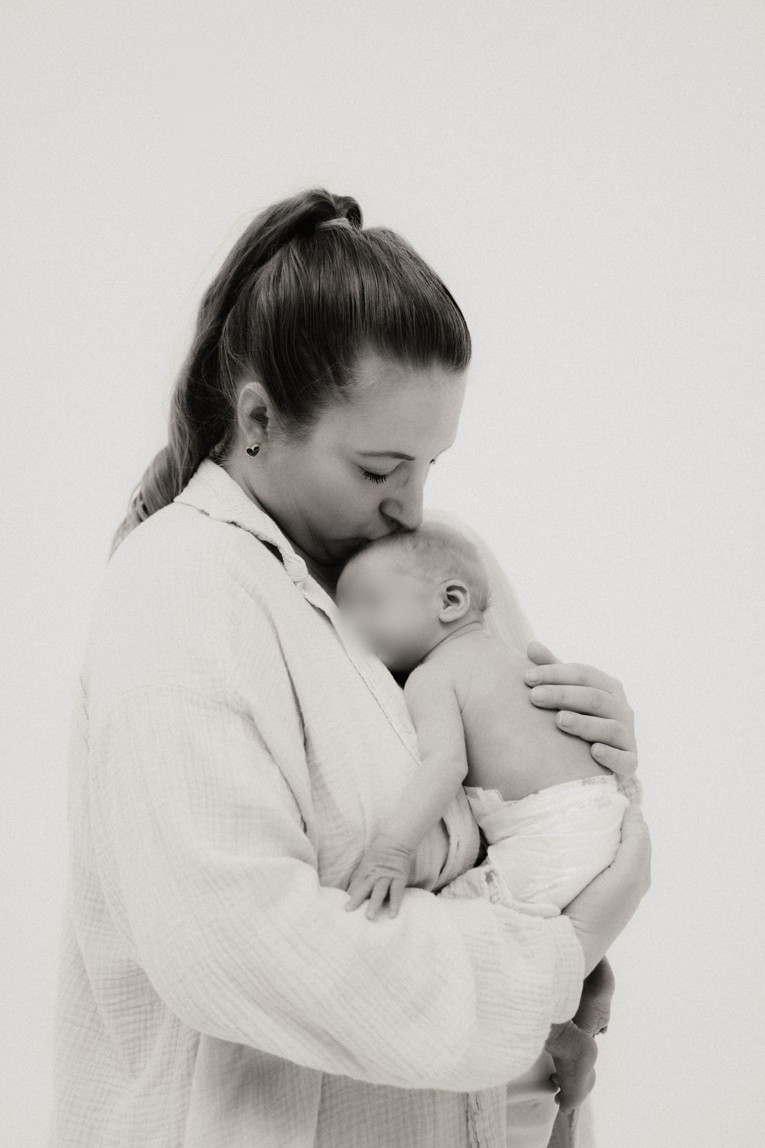 Tender black and white photo of mother in white robe kissing her newborn baby.