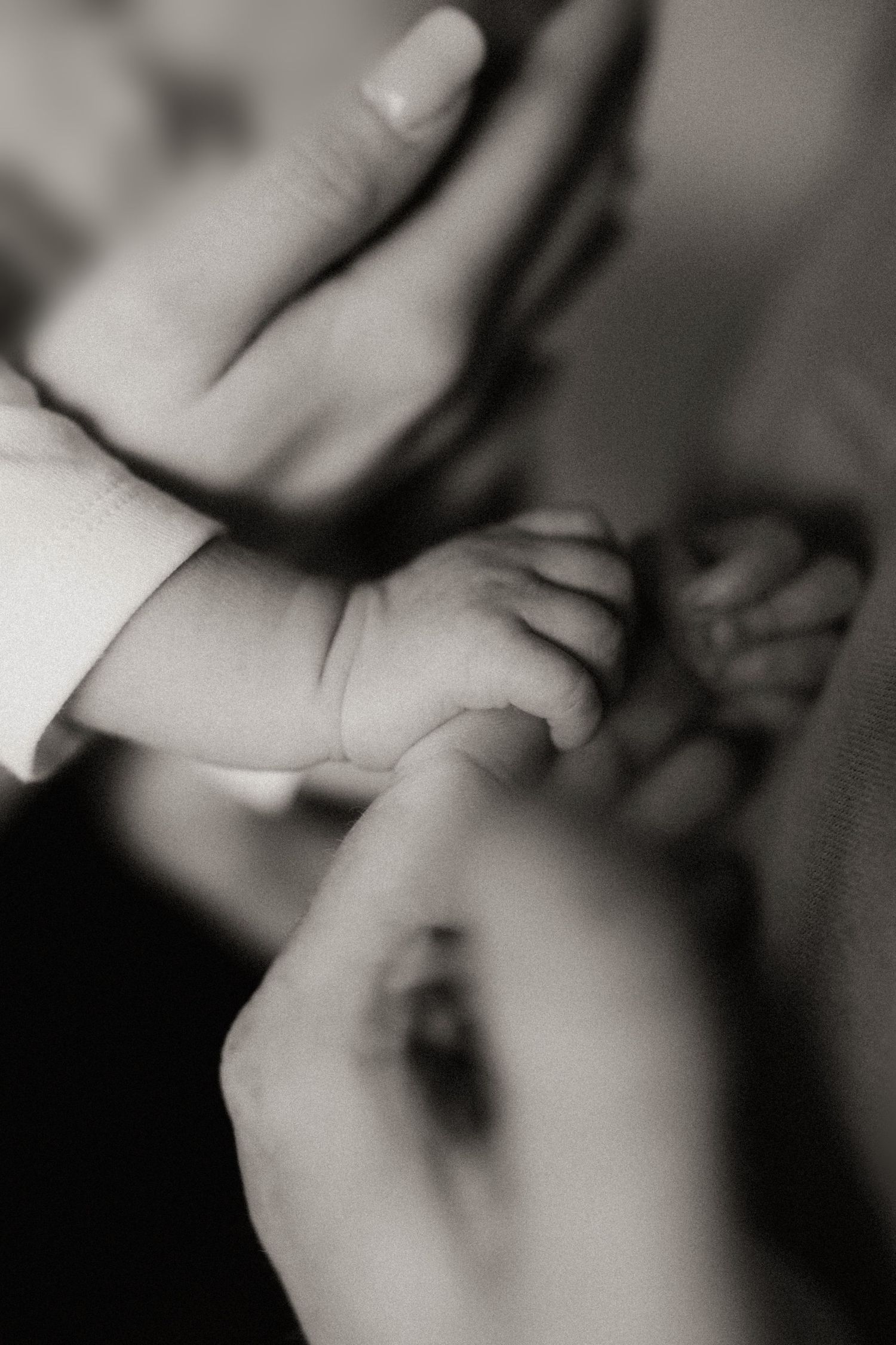 A close-up black and white photograph shows tiny baby fingers being gently held by adult hands.