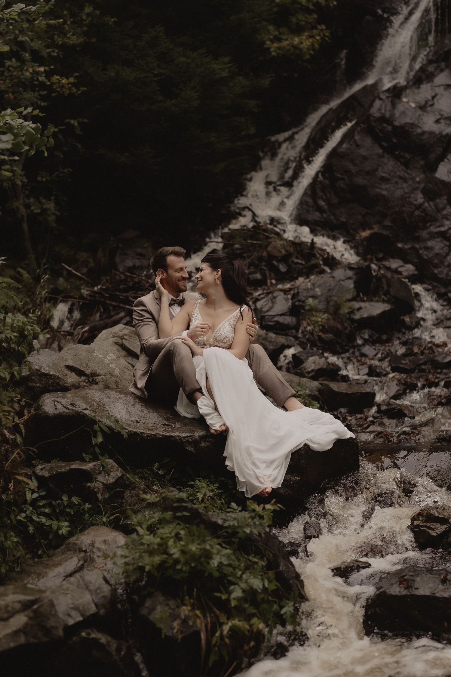 A romantic wedding photoshoot by a cascading waterfall with dark moody tones and rocky terrain.