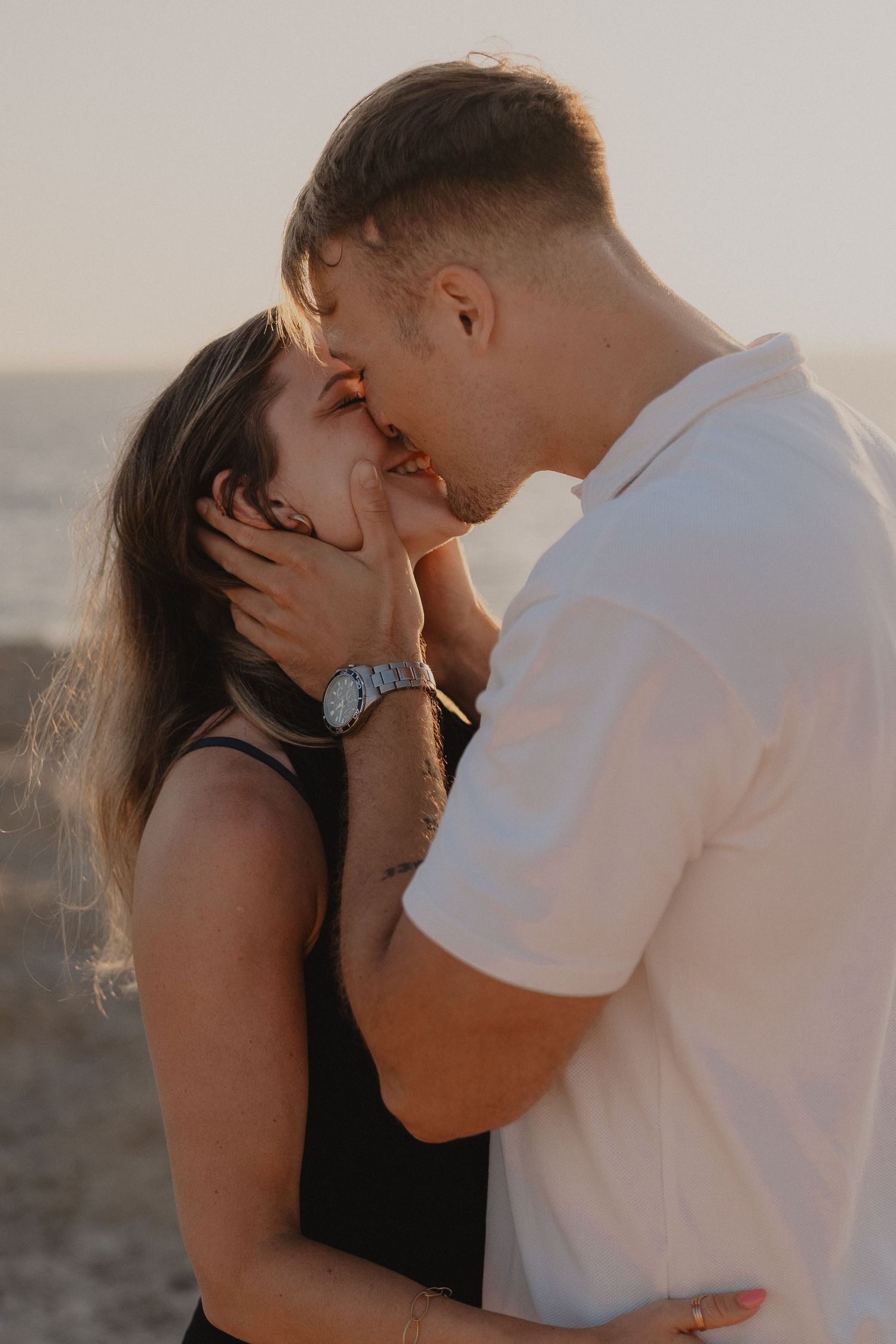Romantic couple sharing a tender kiss on the beach at sunset, man in white shirt gently holding woman's face.