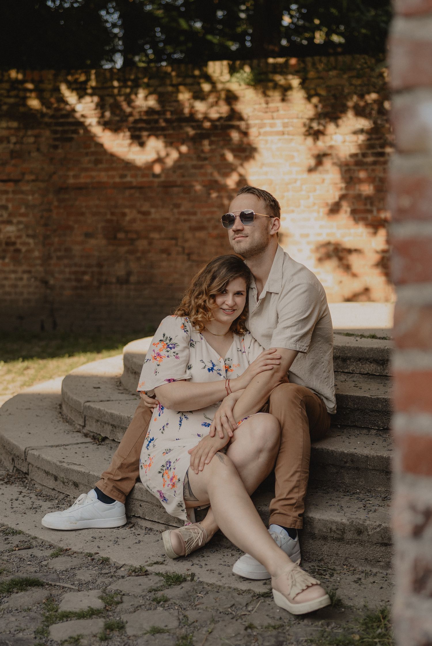 Couple relaxing on stone steps during sunset with brick wall backdrop.
