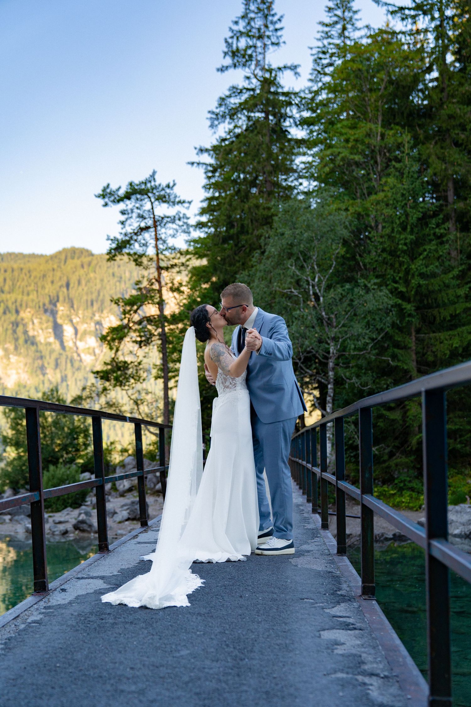 A romantic wedding couple shares a tender moment on a scenic mountain overlook with evergreen trees in the background.