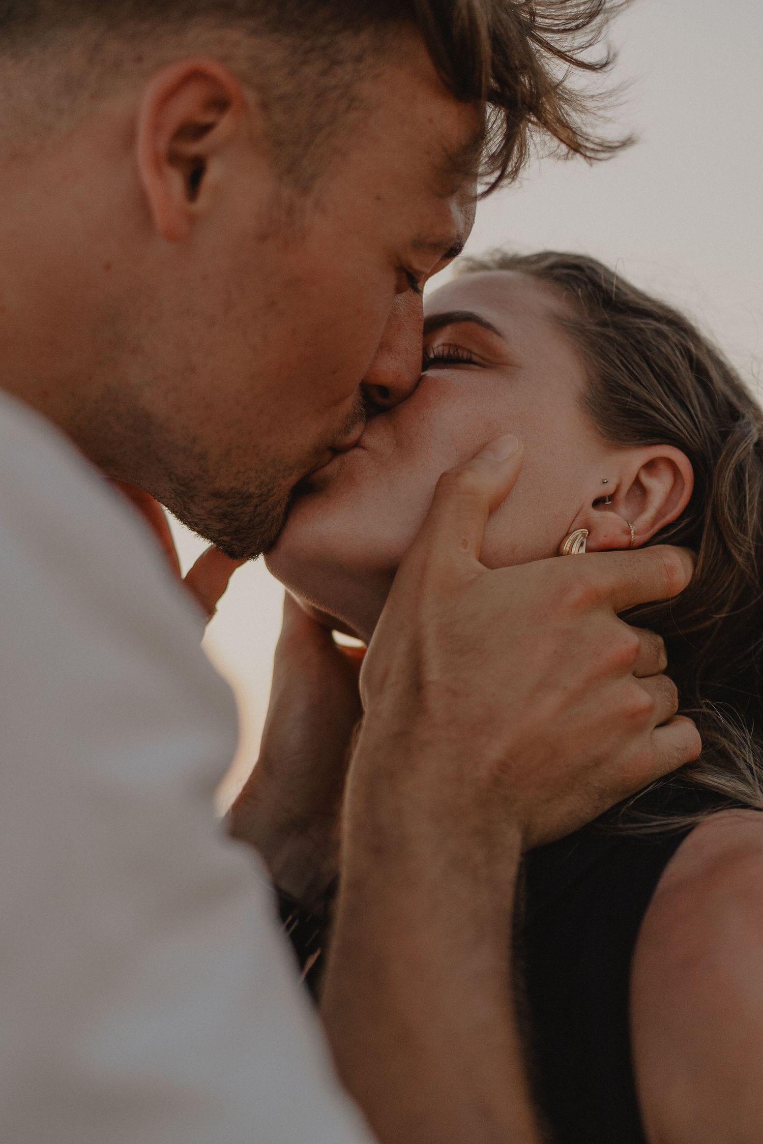A couple sharing a tender kiss, with the man gently cradling the woman's face in a romantic outdoor setting.