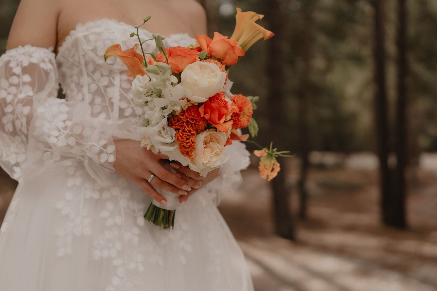 Close-up of orange wedding bouquet details against a white lace wedding dress.