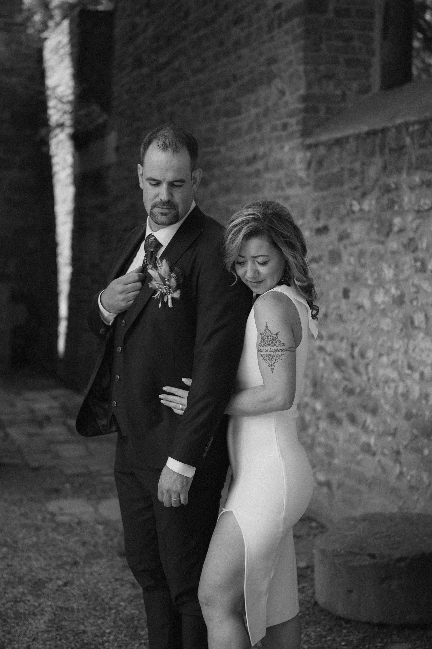 An artistic black and white portrait of a couple in wedding attire against a brick wall backdrop.