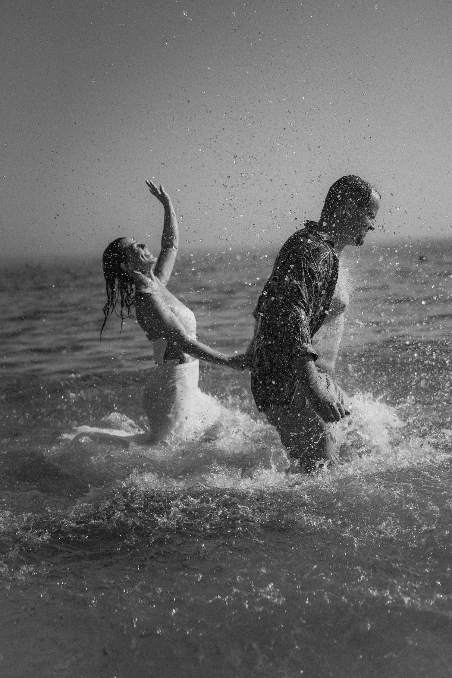 Black and white photo of people playing and splashing in ocean waves.