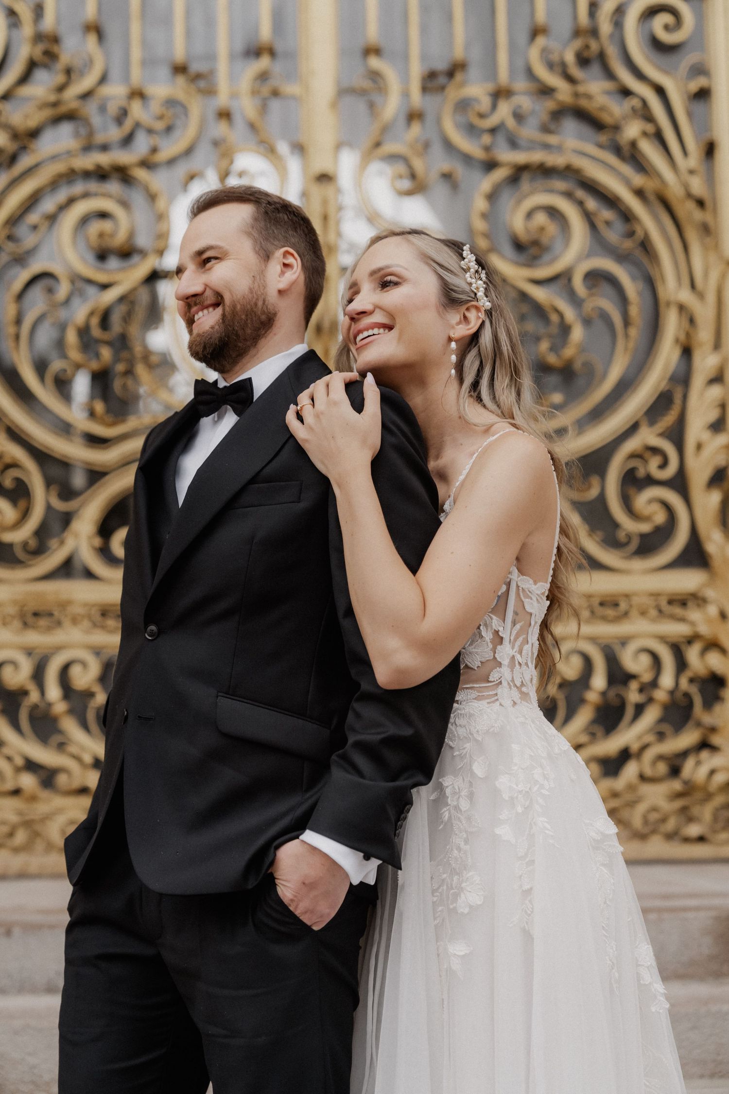 Joyful wedding moment captured against intricate golden gates and architectural details.