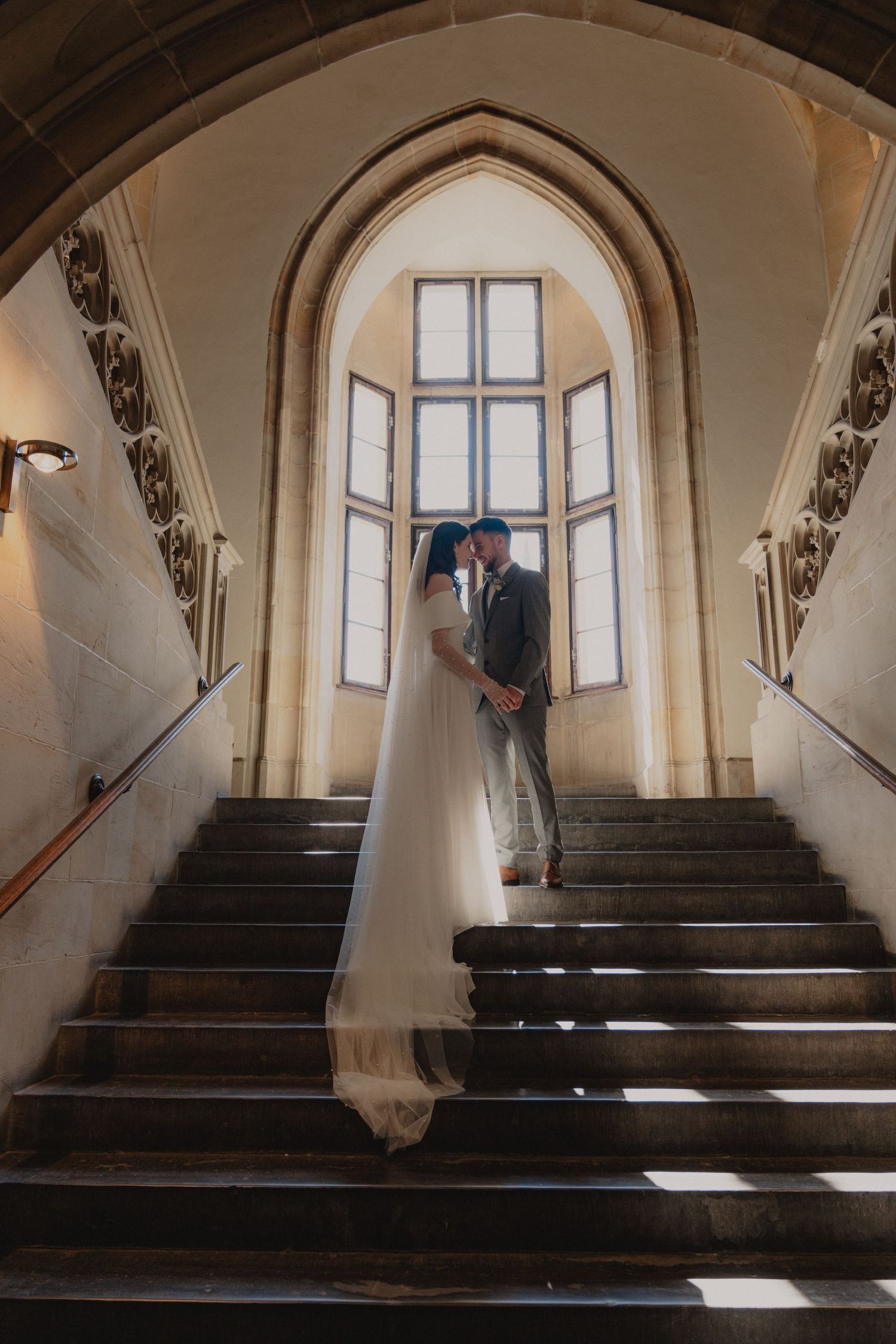 Elegant wedding portrait on historic stone staircase with arched window and natural light.