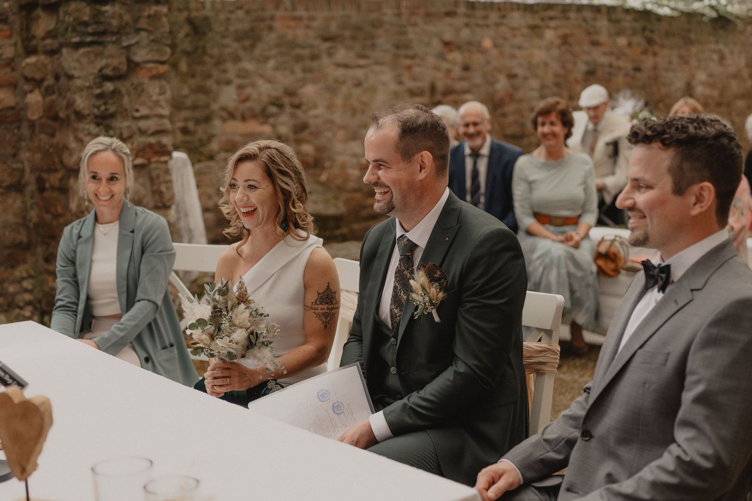 Wedding guests seated at outdoor reception venue with exposed brick walls and rustic decor.