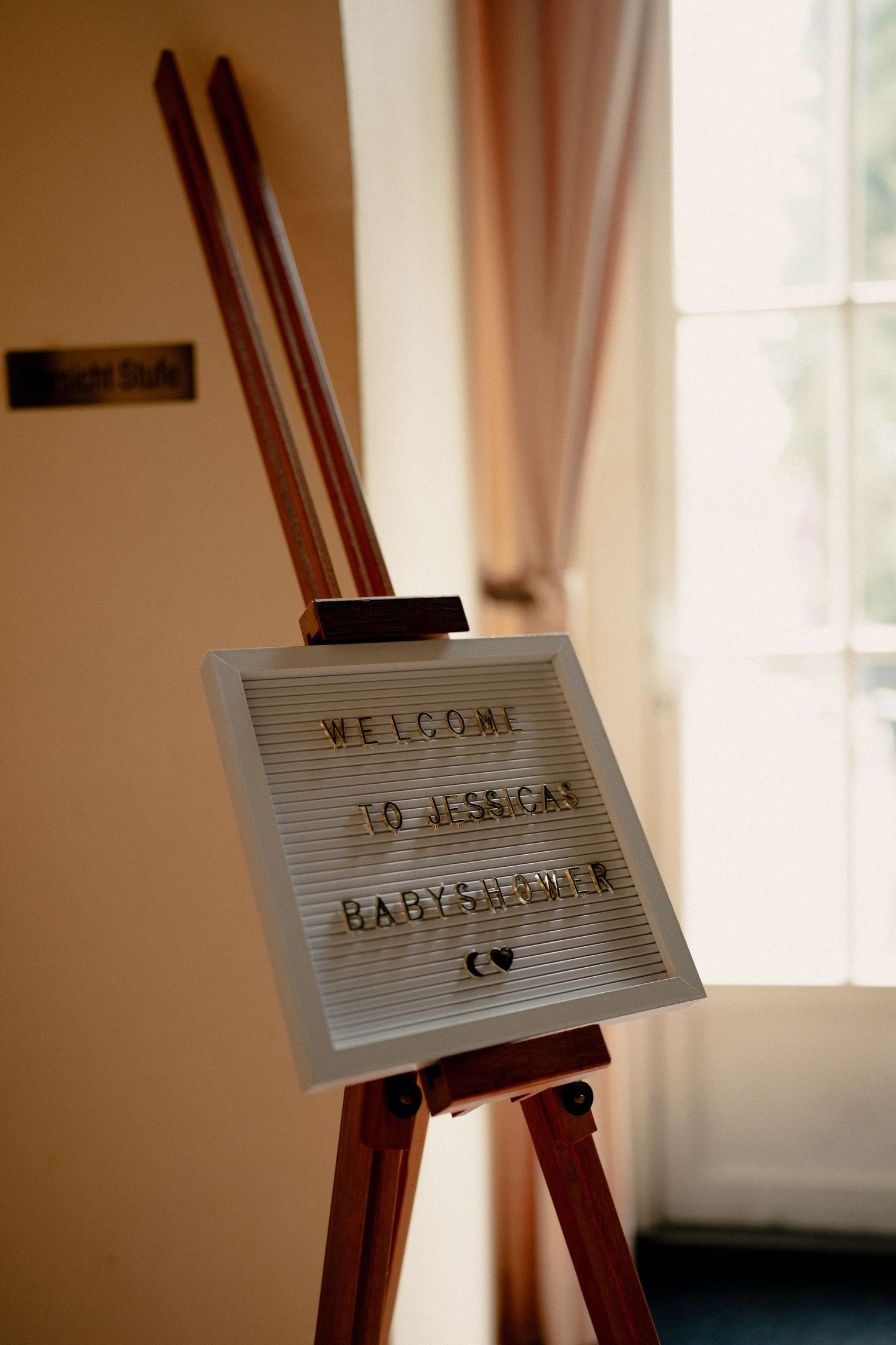 A wooden easel displays a letter board sign reading Welcome to Jessica's Baby Shower at an elegant venue.