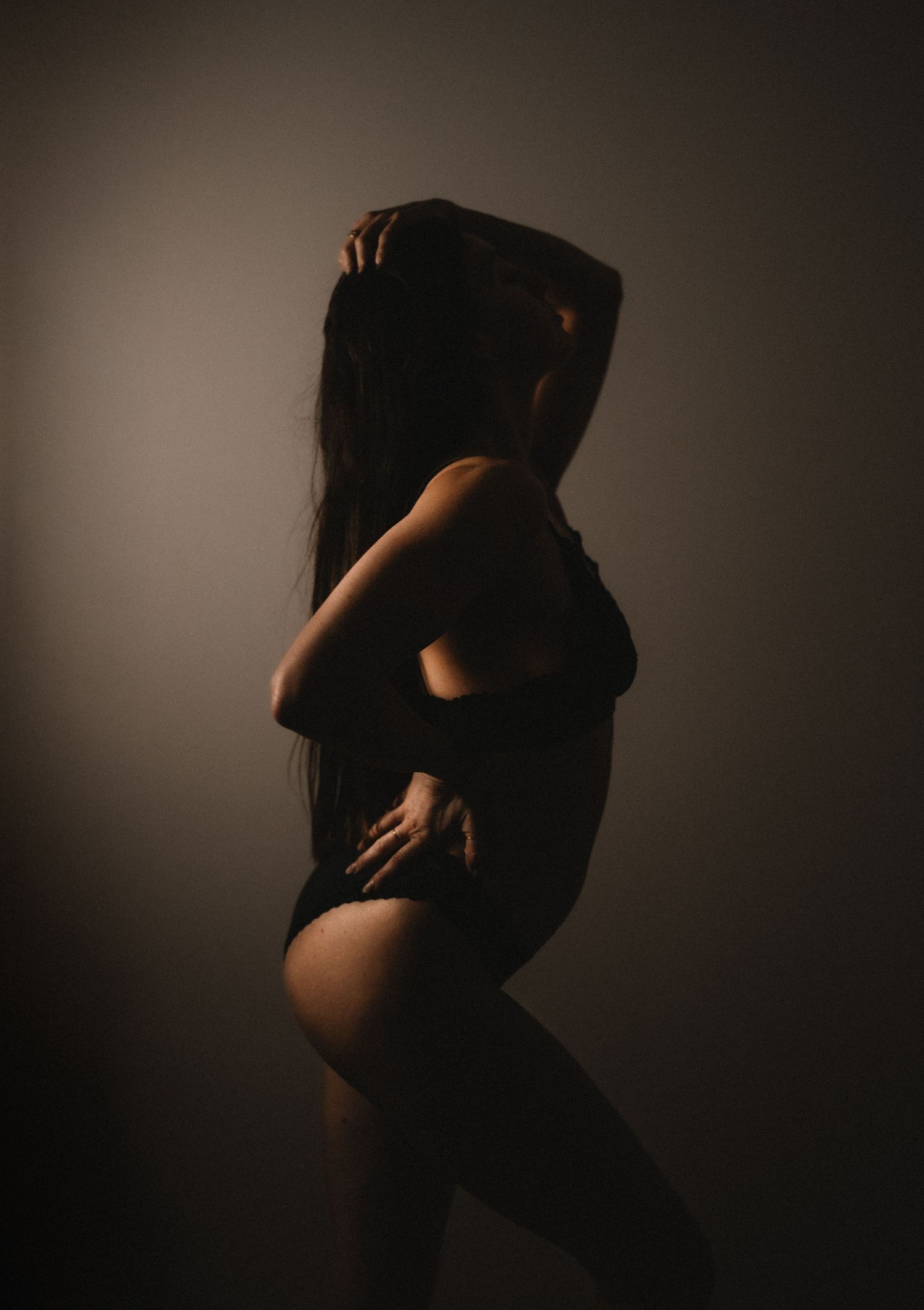 A silhouetted figure in black clothing poses dramatically against a dark background with moody lighting.