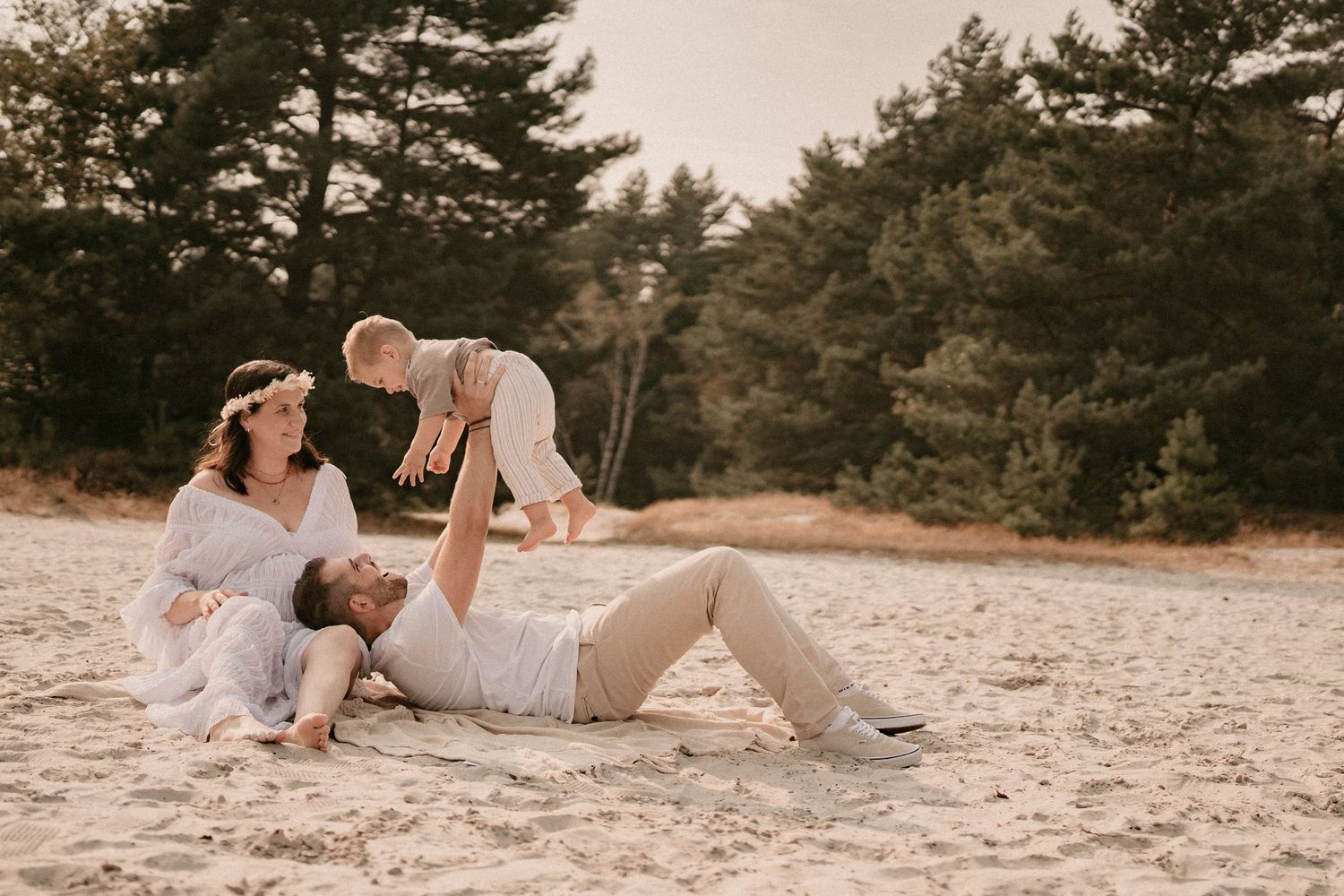 Couple in light colored clothing relaxing on sandy beach during golden hour.