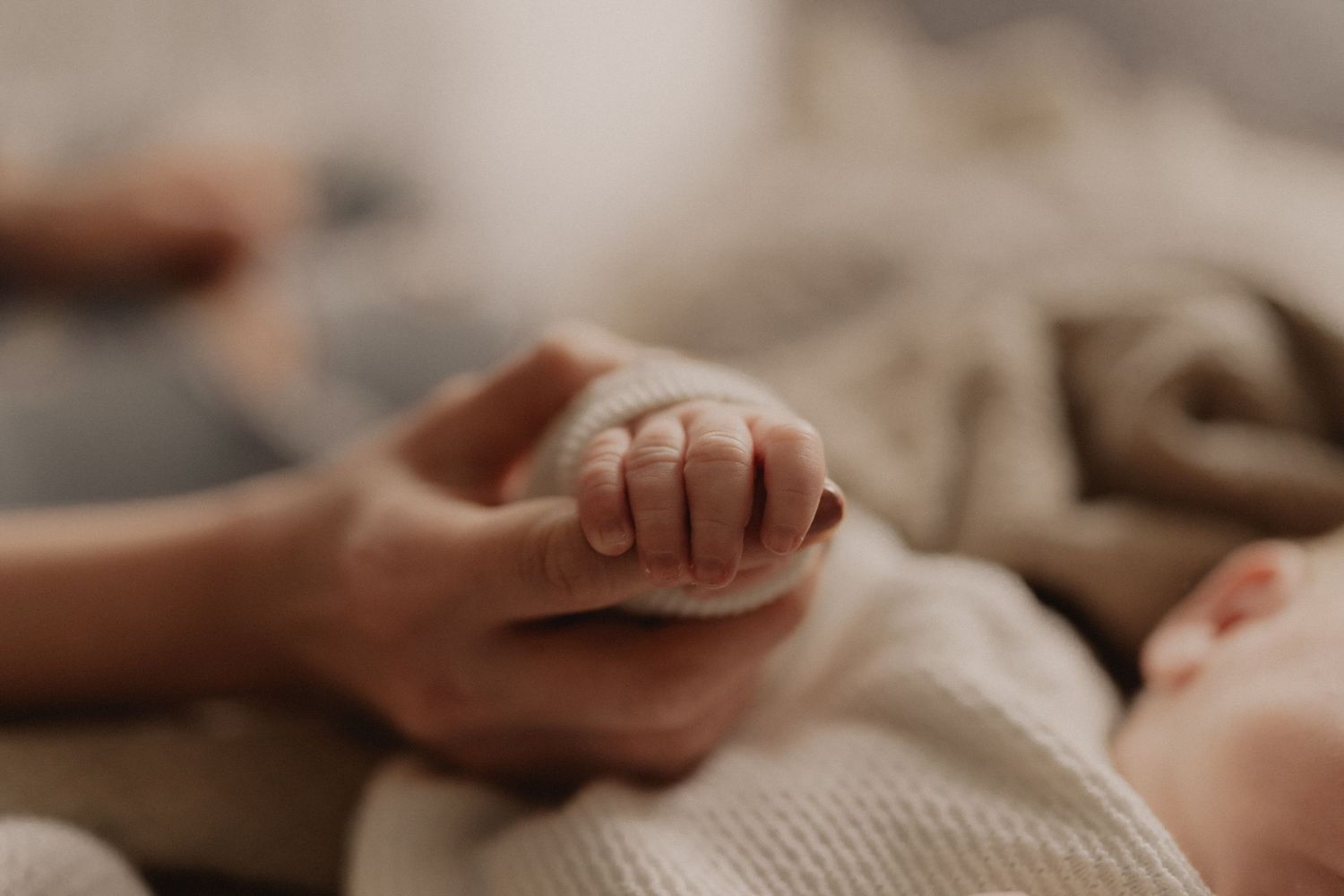 Gentle hands touching baby feet on soft textured fabric.
