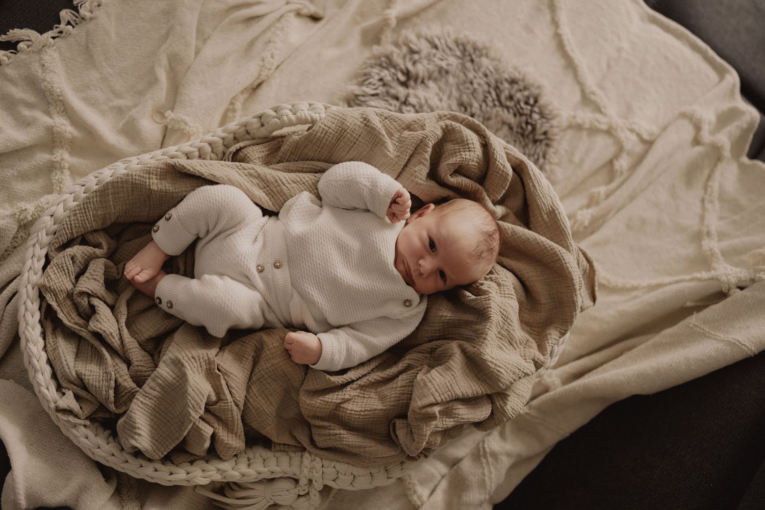Peaceful newborn baby sleeping in a woven basket surrounded by soft beige blankets in a cozy neutral-toned setting.