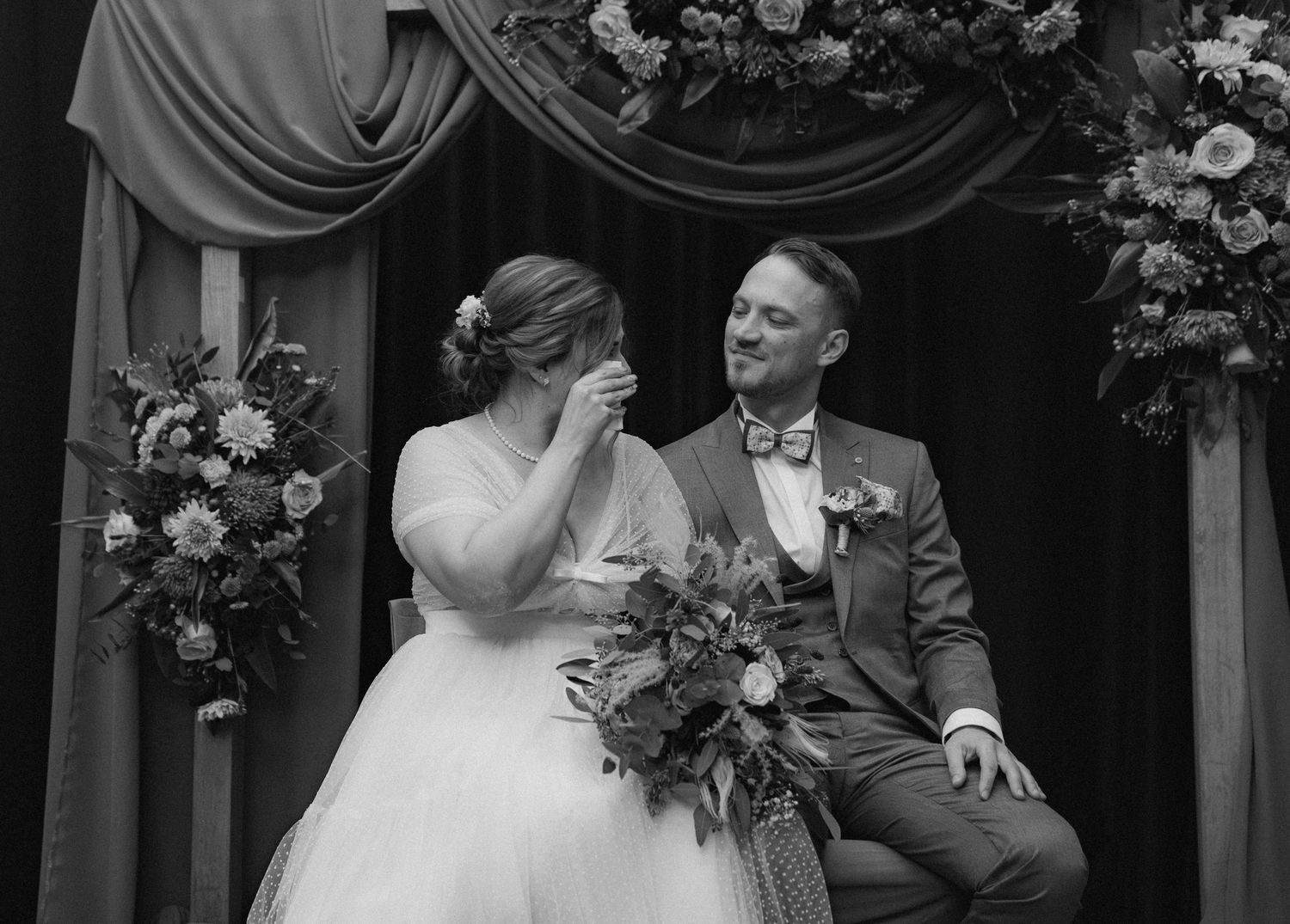 Black and white wedding photo with floral arrangements in elegant indoor setting.