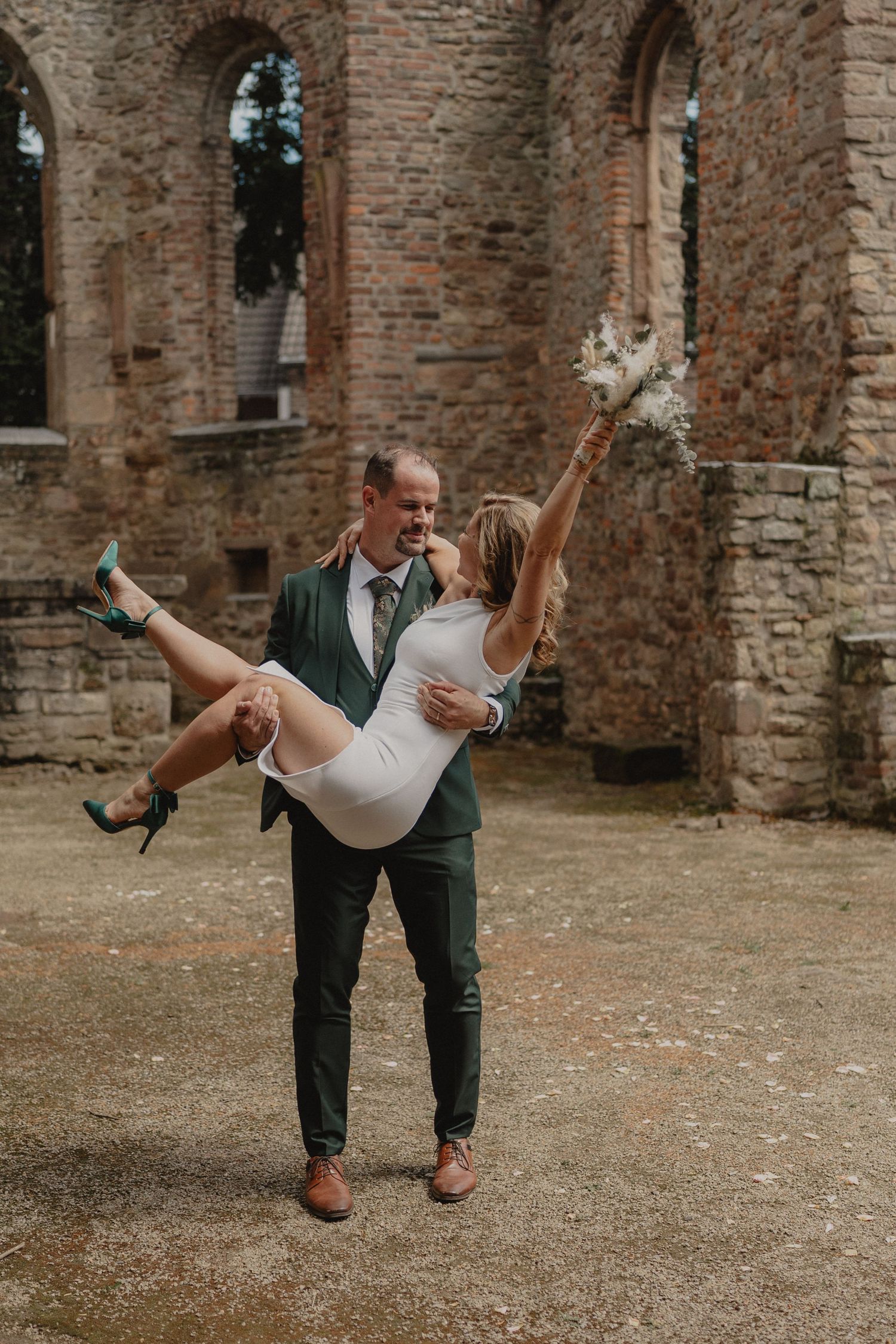 A playful wedding couple poses in front of historic stone ruins while celebrating their special day.