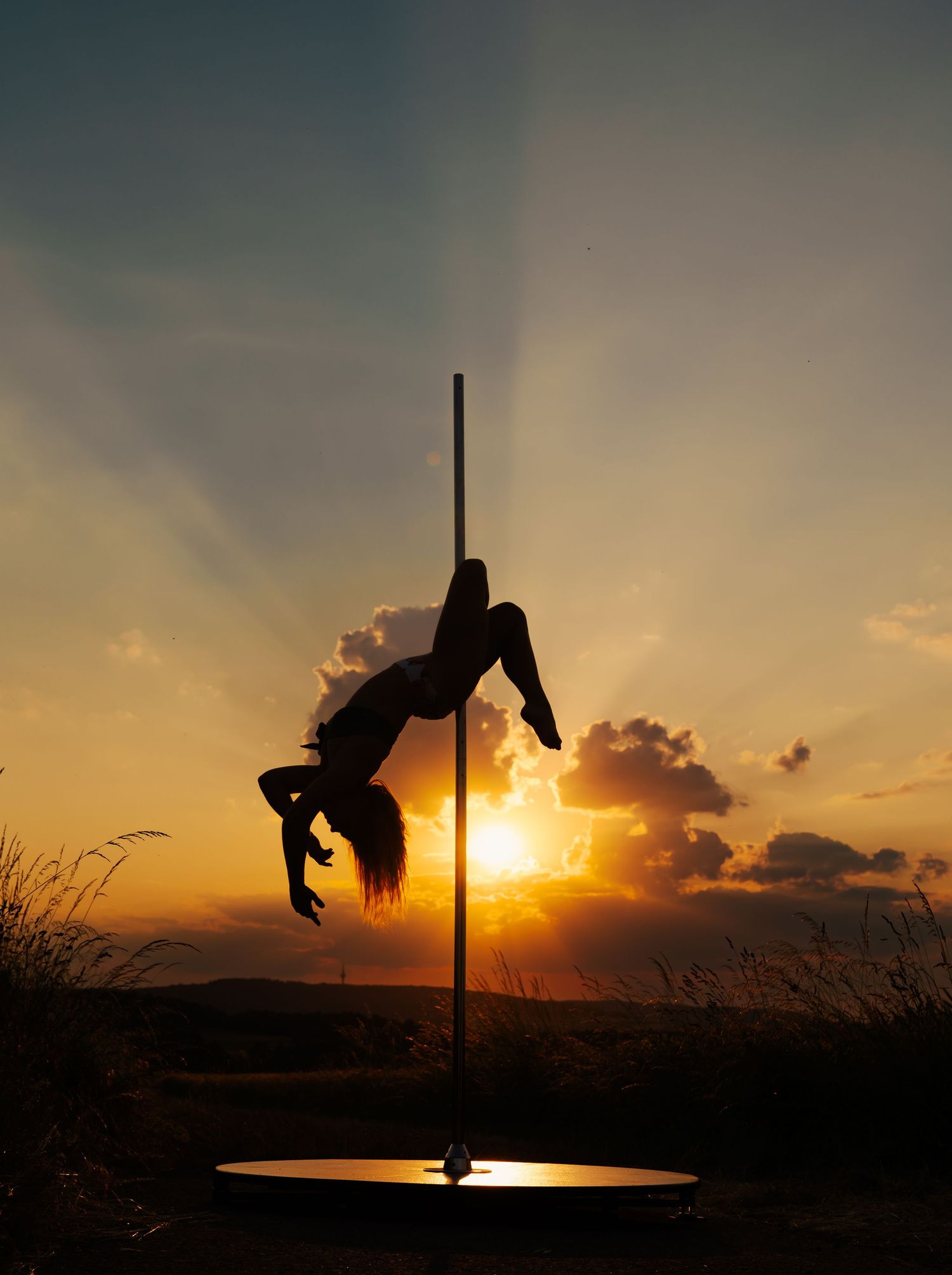 Silhouette of a pole dancer performing an acrobatic move against a stunning golden sunset sky.