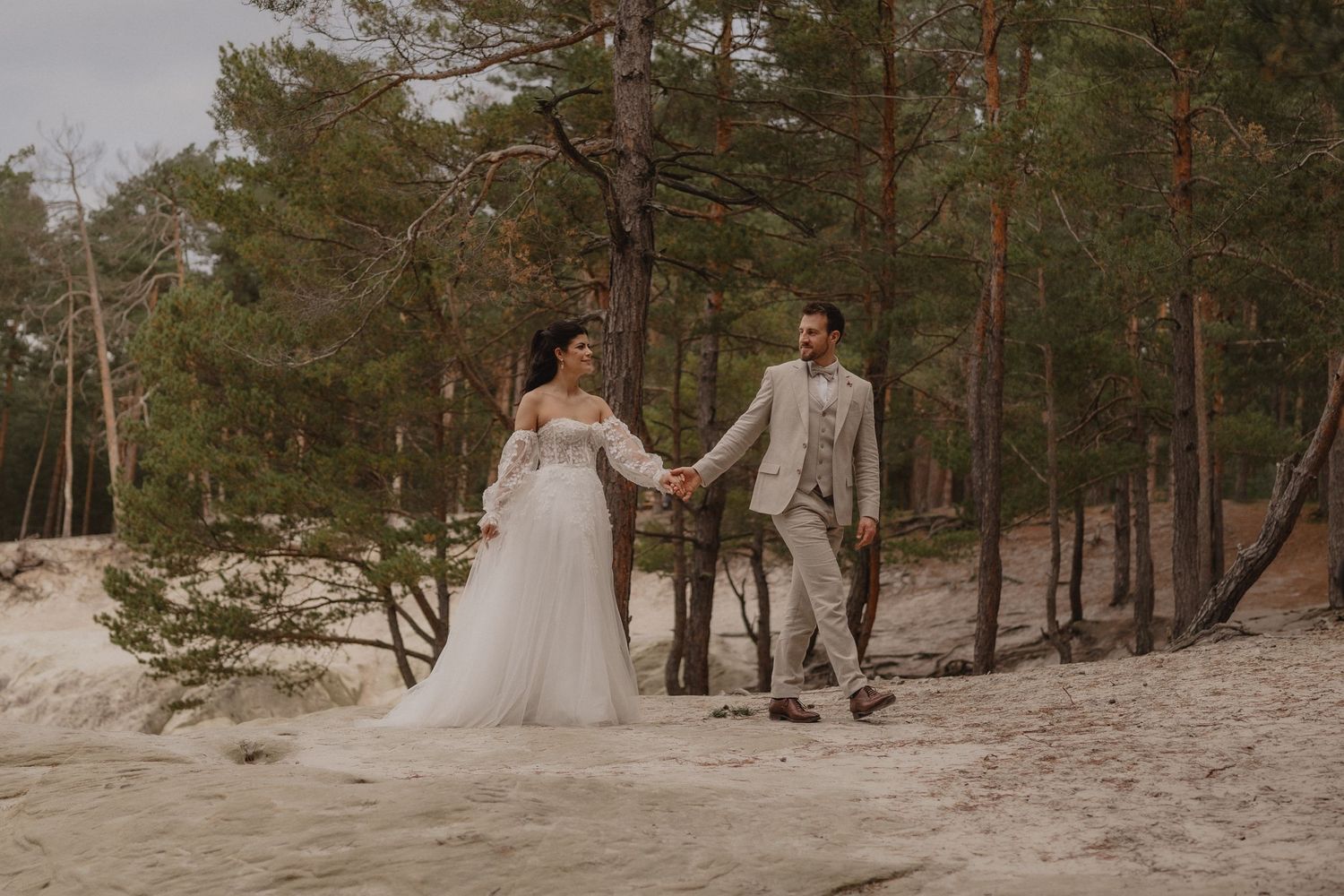 Wide landscape shot of a wedding couple walking through a pine forest setting.