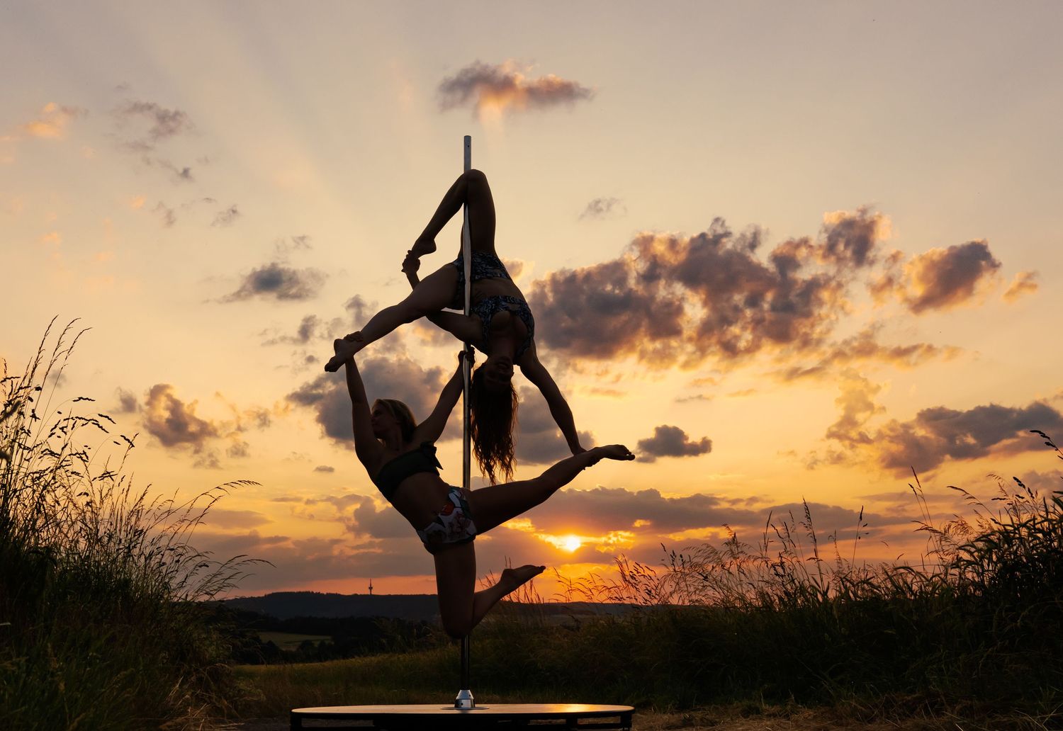 Two acrobats perform a stunning pole dance silhouette against a vibrant golden sunset sky.