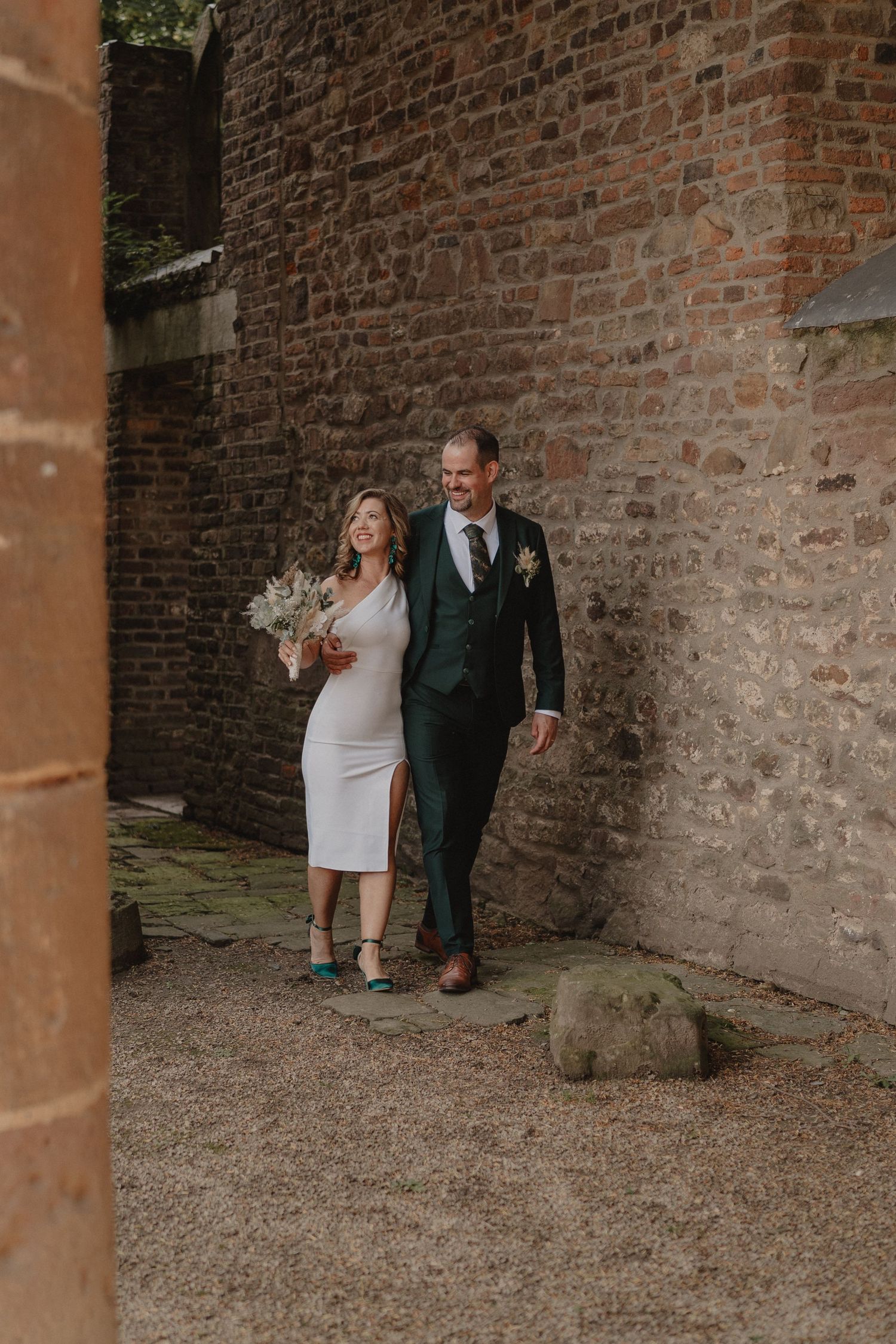 Wedding couple playfully poses against historic brick walls and stone columns.