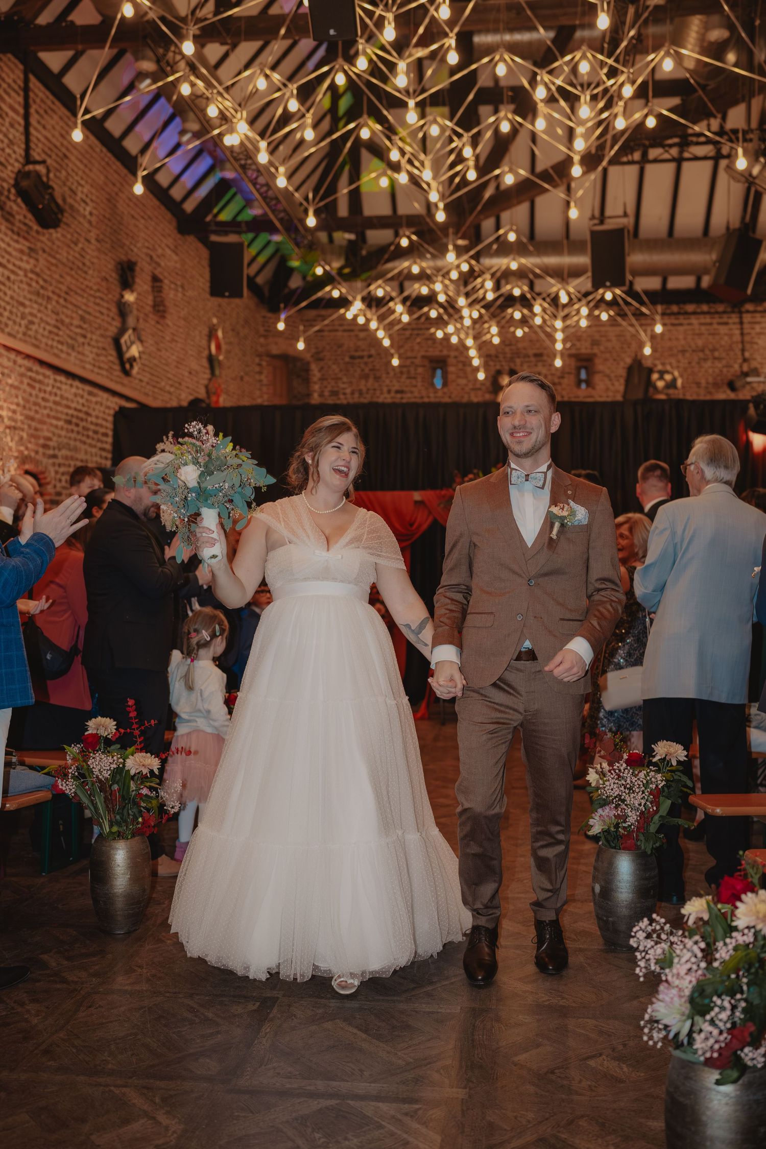 Wedding reception dance floor with string lights and couples dancing in a rustic brick venue.
