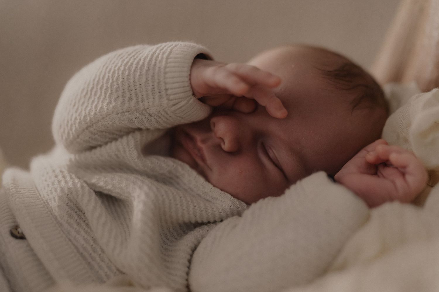 Close-up of a sleeping baby wearing a soft knit sweater in neutral tones.