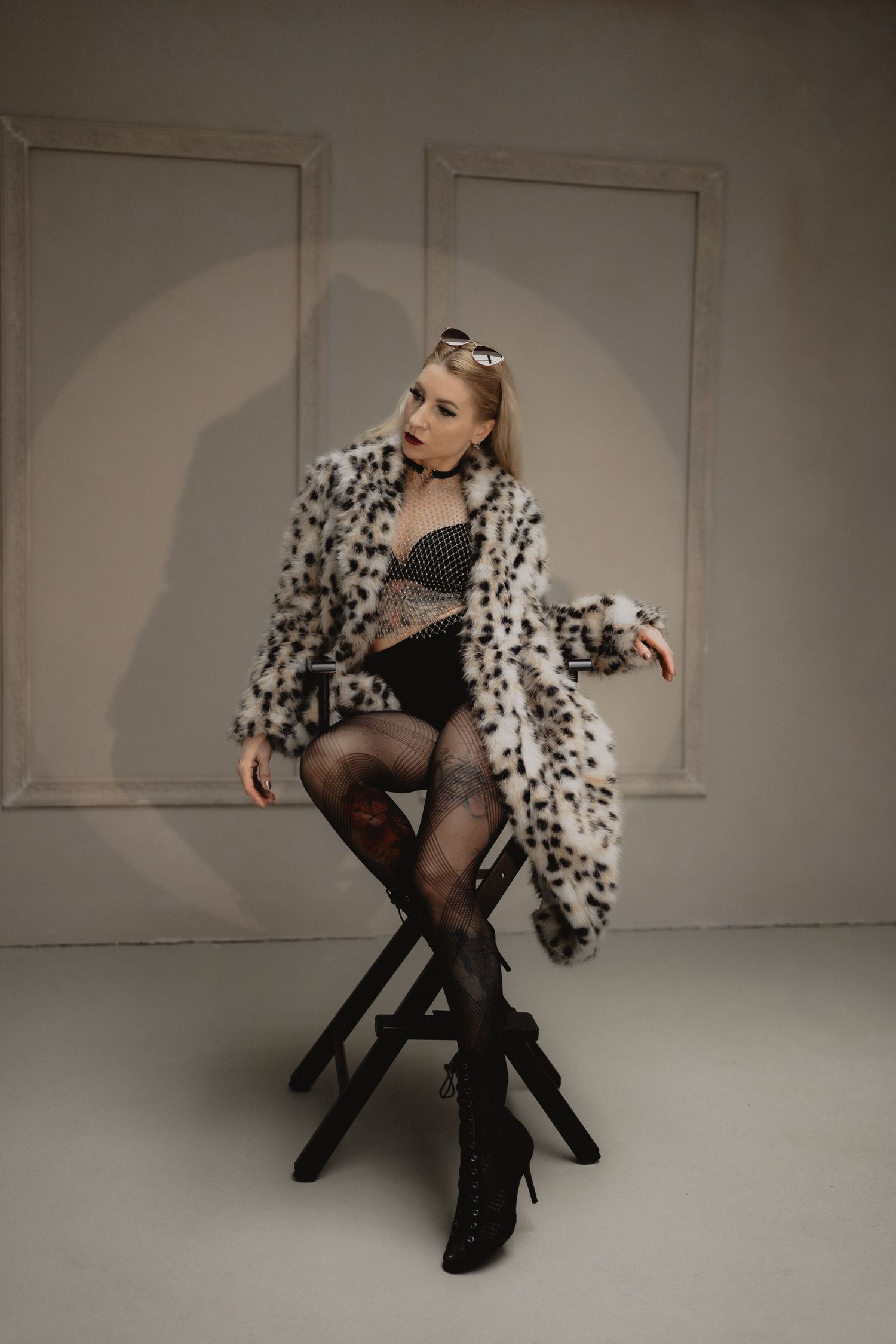 Fashion model poses in black and white polka dot coat and sheer stockings on white backdrop in artistic photo series.