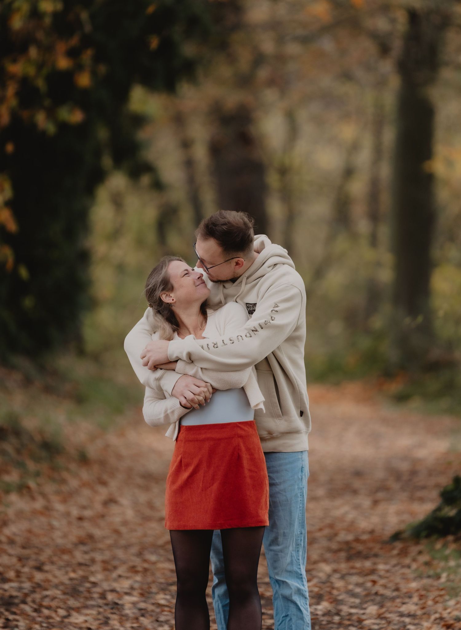 A couple shares a romantic moment among fallen autumn leaves in a park setting.